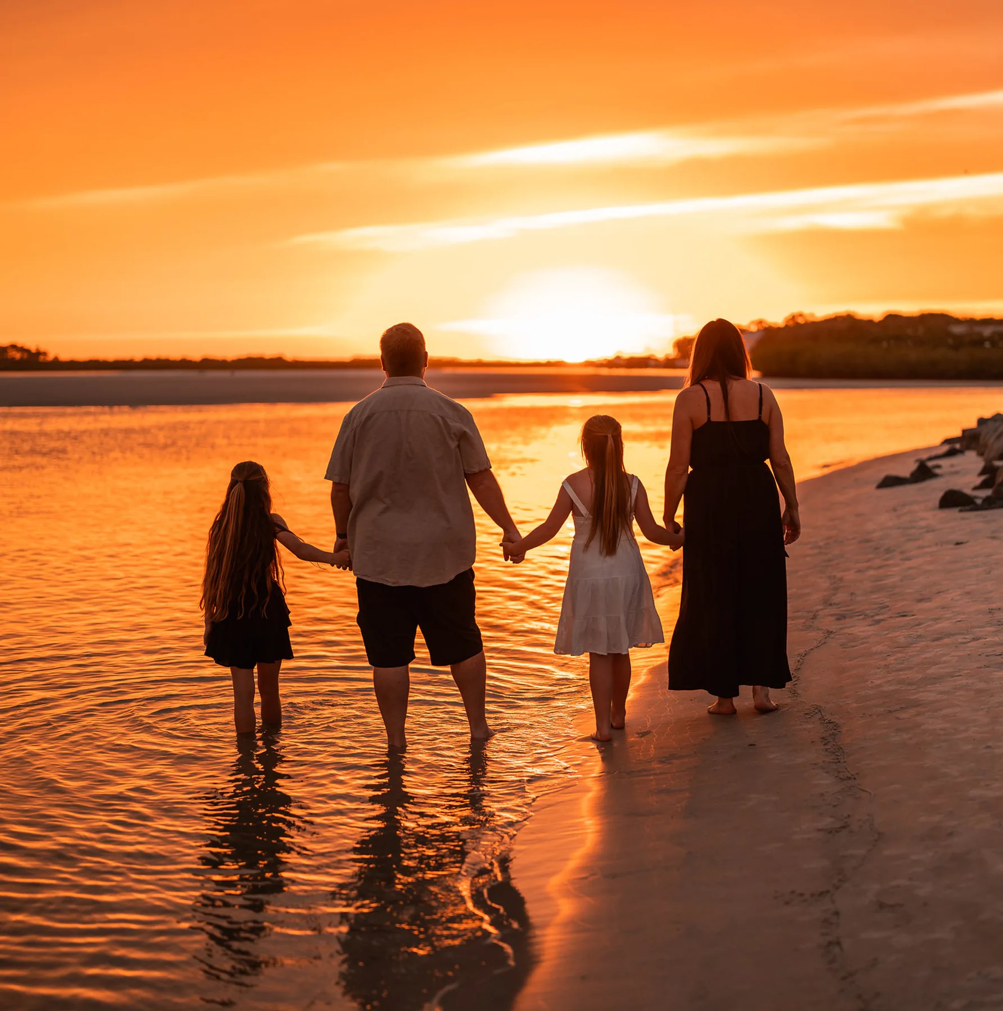 Family standing together in the water at sunset during a Ponce Inlet beach family photo session.