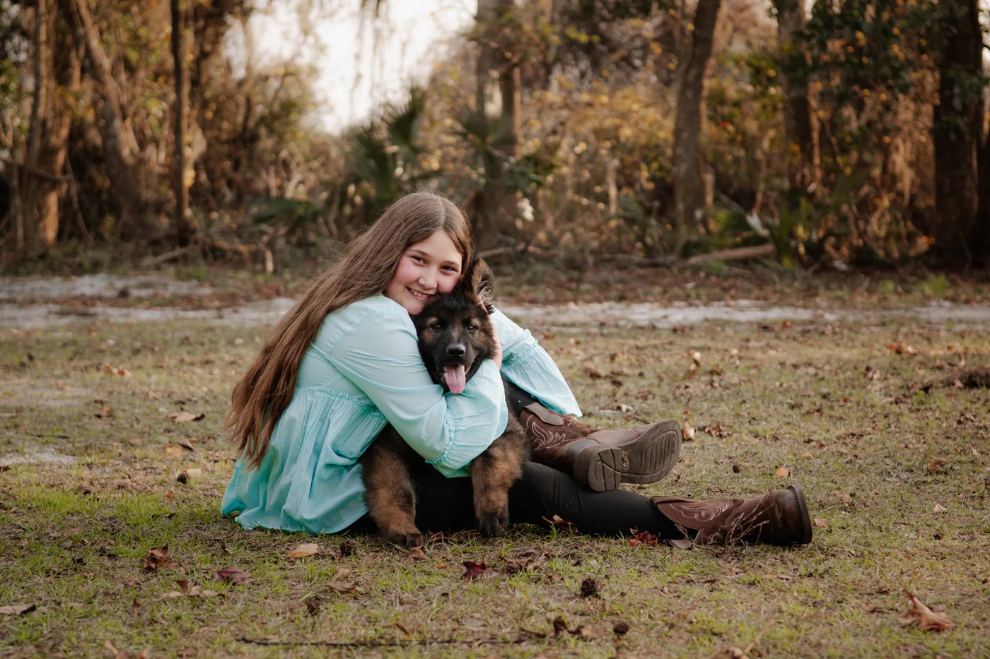 Young woman hugging a fluffy black dog while seated on the grass.