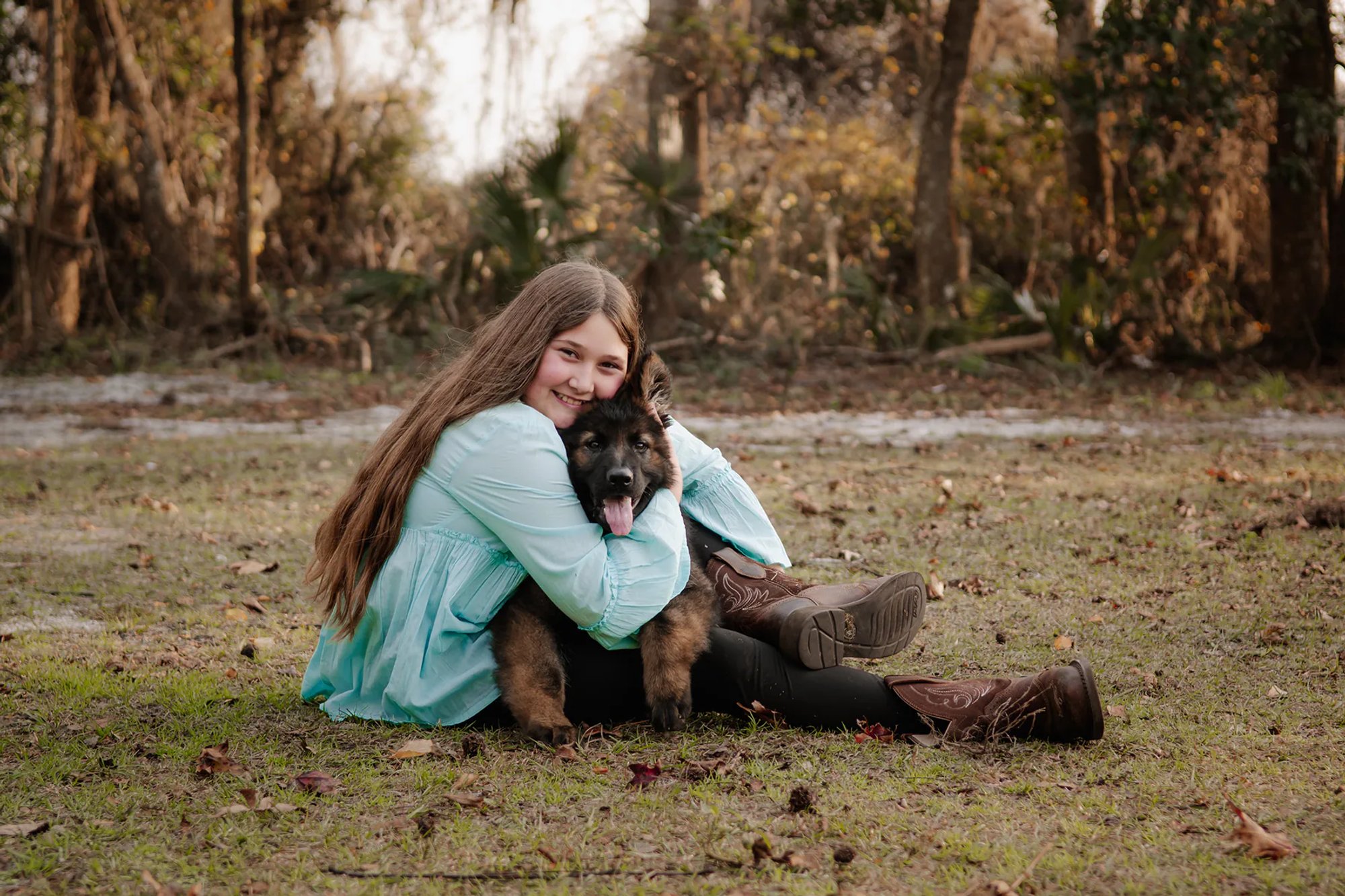 Young woman hugging a fluffy black dog while seated on the grass.