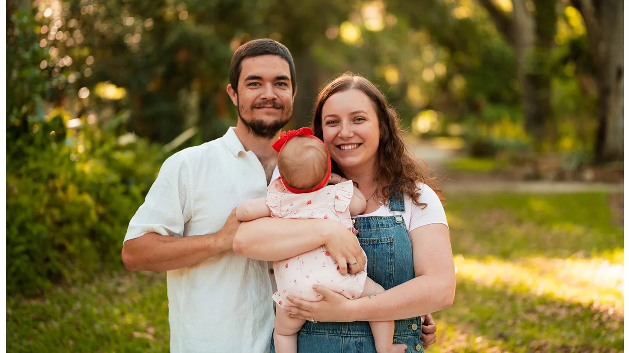 Parents holding their baby during a sunlit outdoor family portrait.