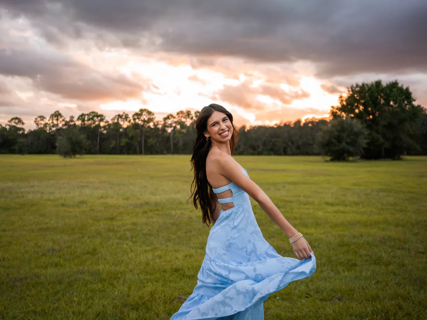 Young woman twirling a pale blue dress across an open field.