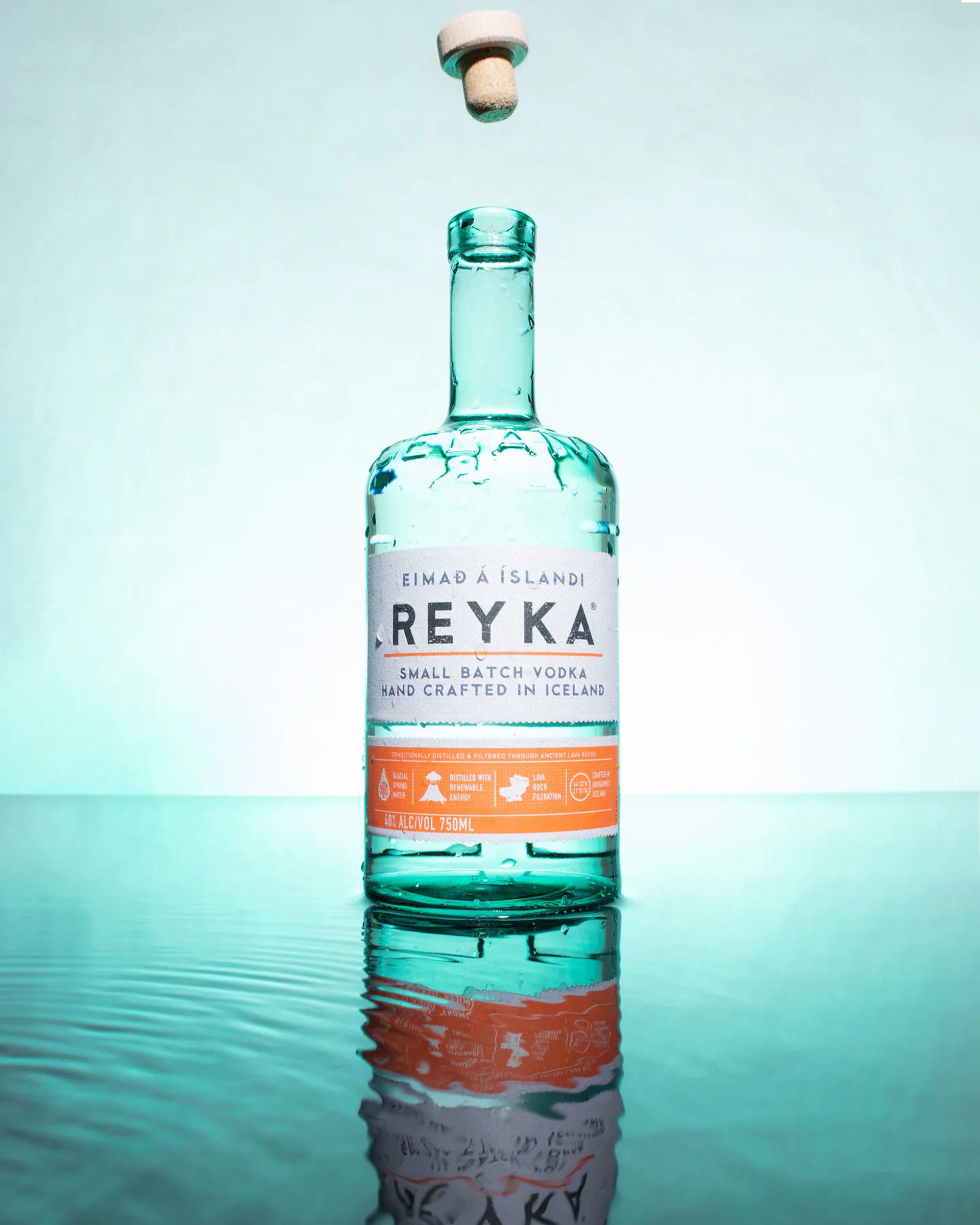 Reyka vodka bottle reflected on a glossy teal surface.