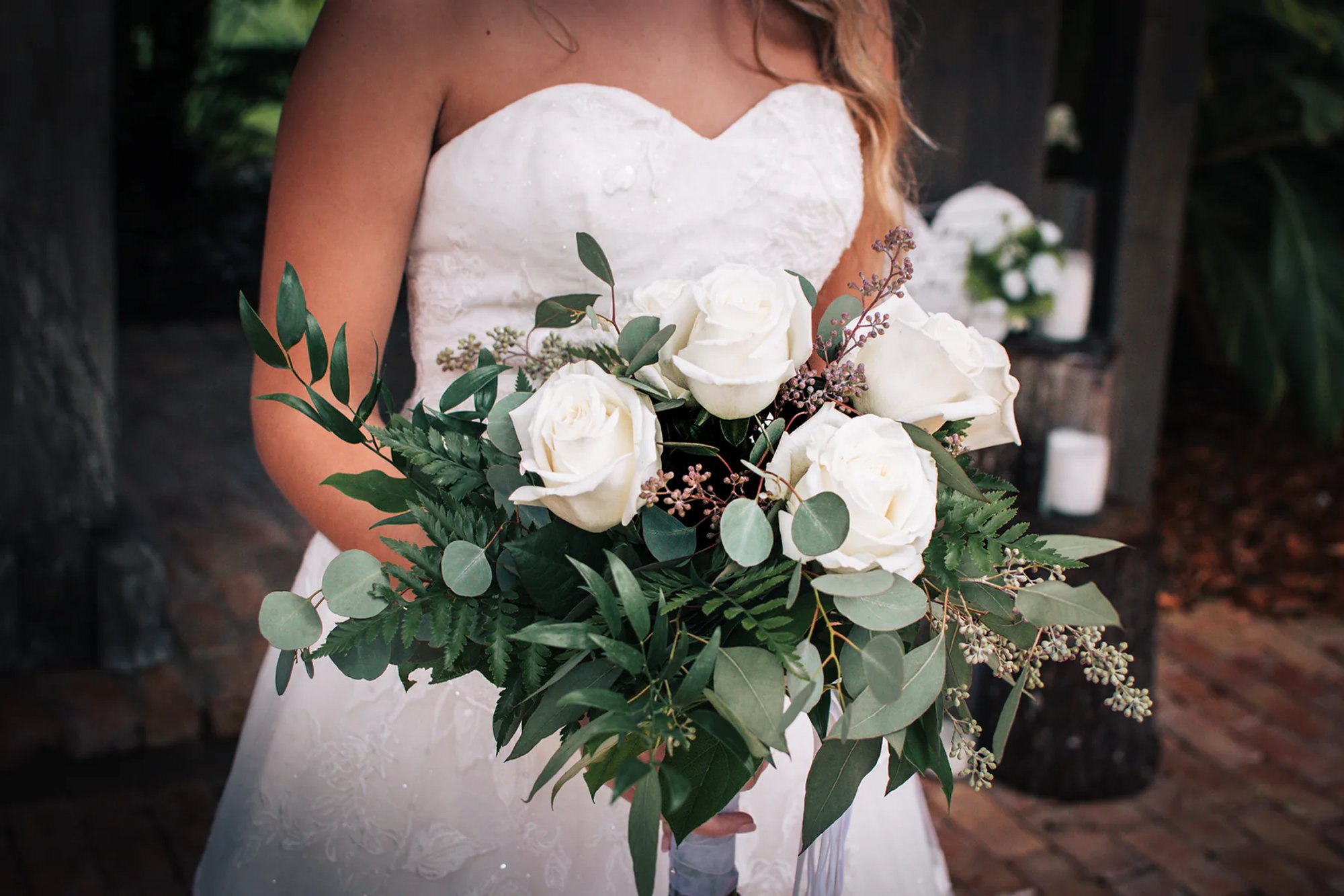 Bride holding a bouquet of white roses and greenery.