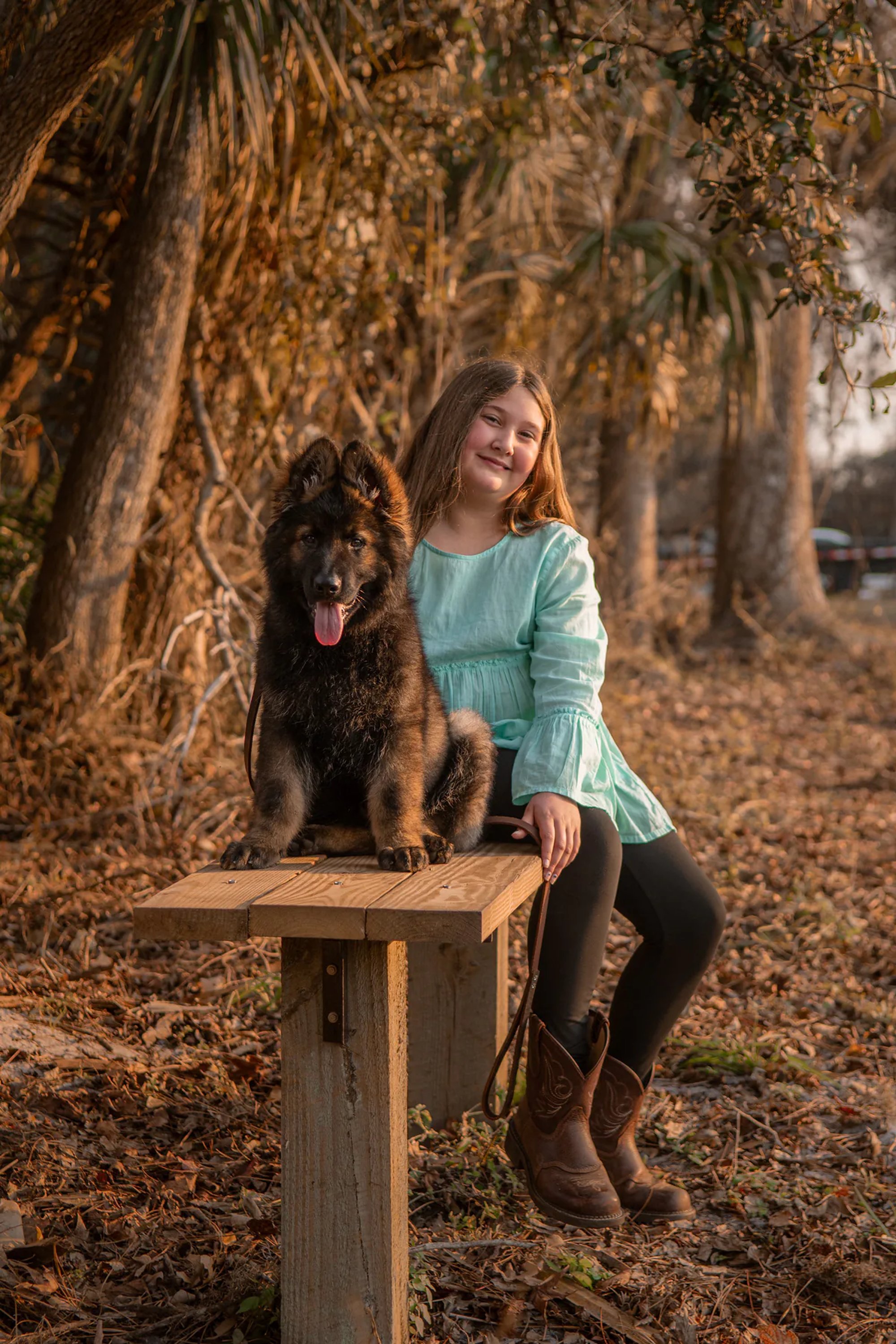Young woman seated with her black dog on a rustic wooden bench.