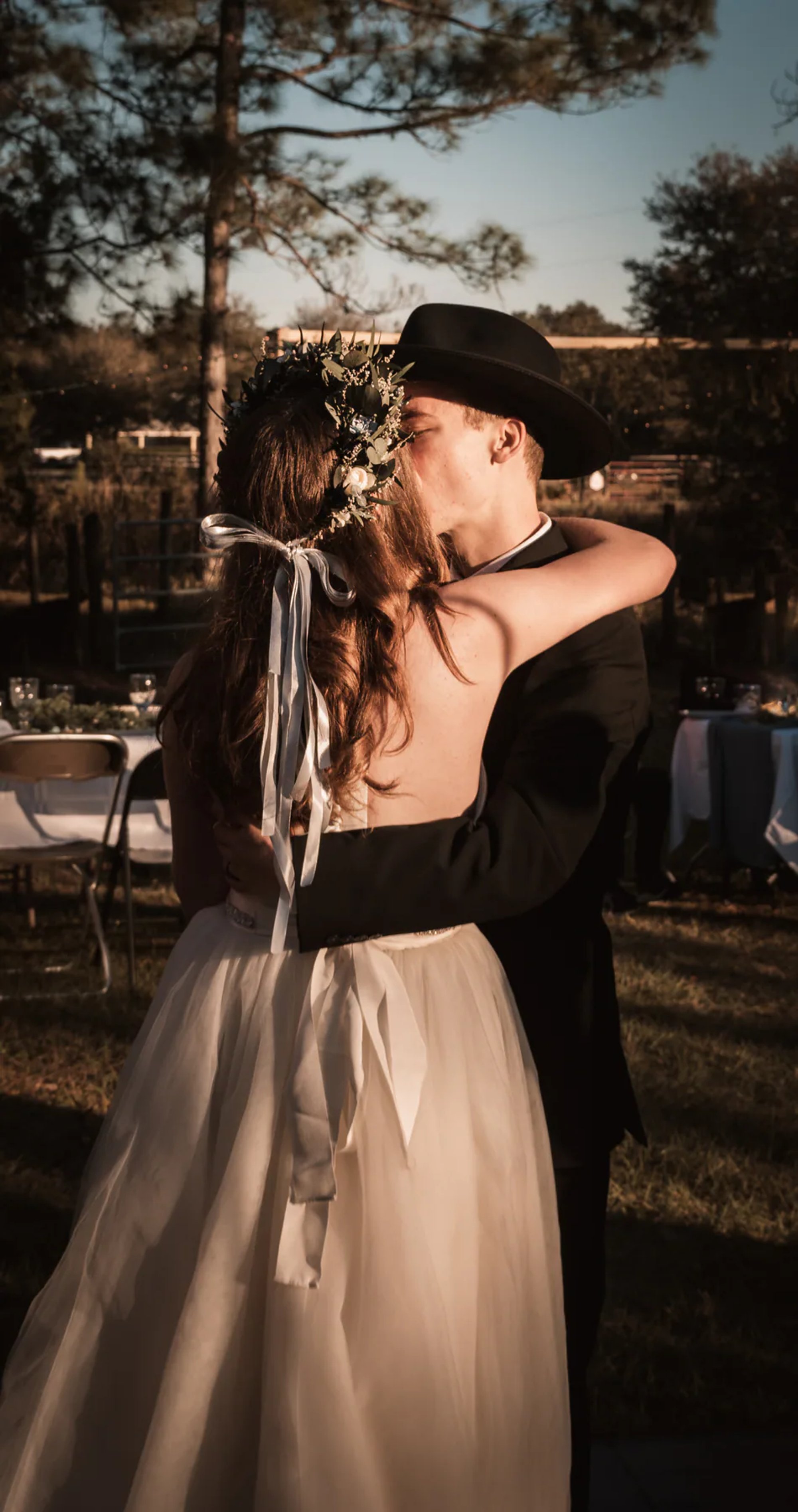 Bride and groom embracing outdoors near a wooden fence.