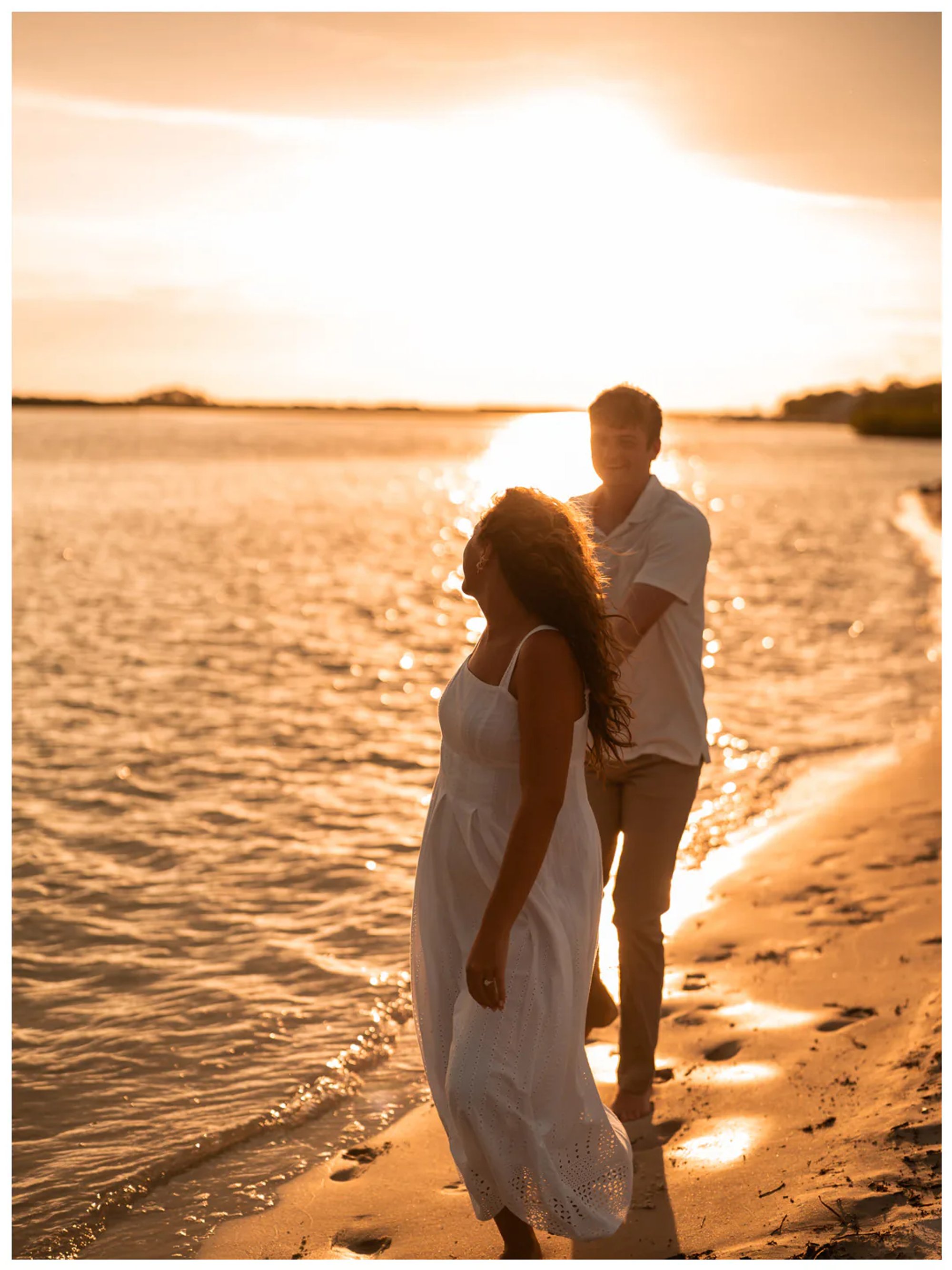 Couple walking together along the sunlit shoreline.