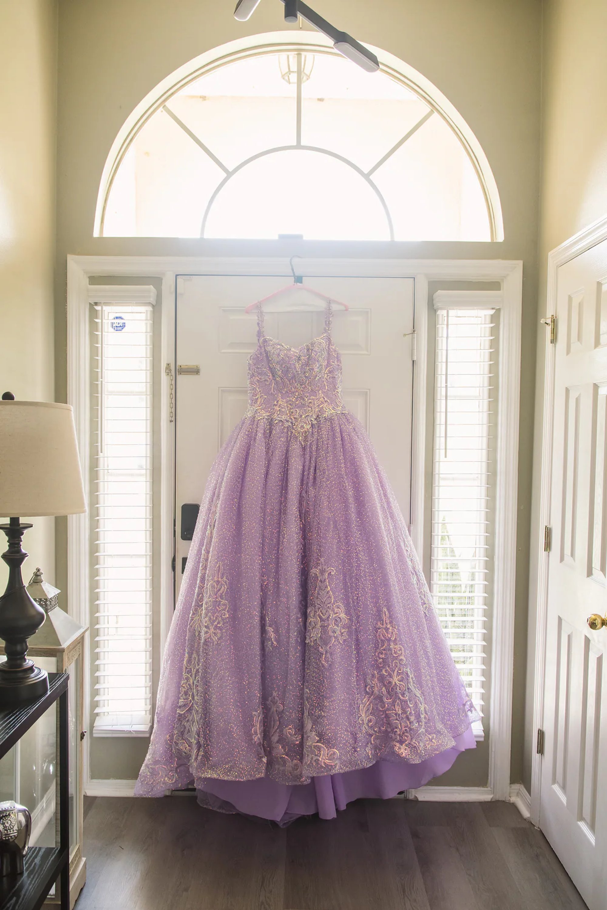 Purple quinceañera ball gown hanging in a bright entryway.