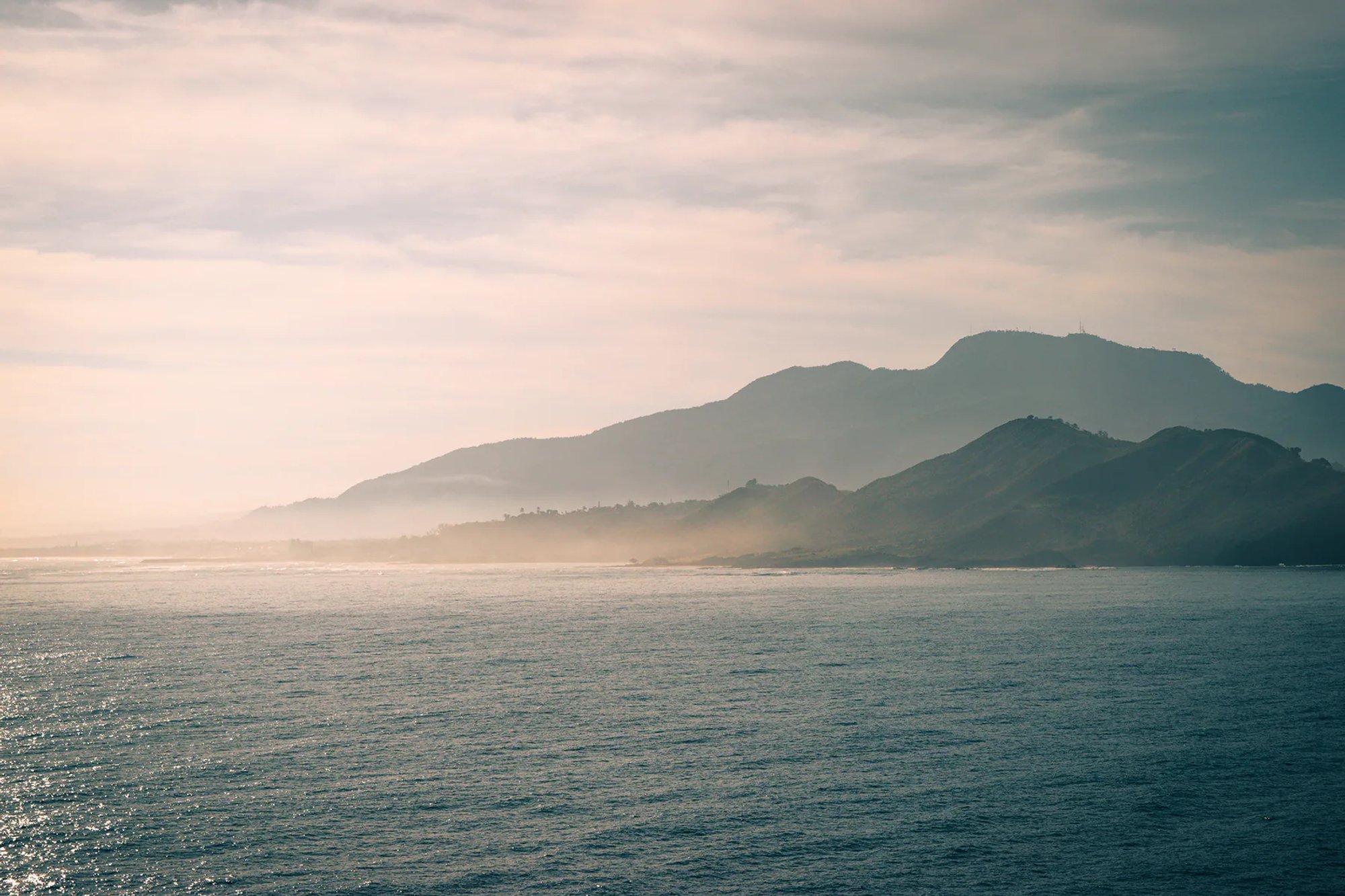 Mountainous coastline viewed across calm blue water.