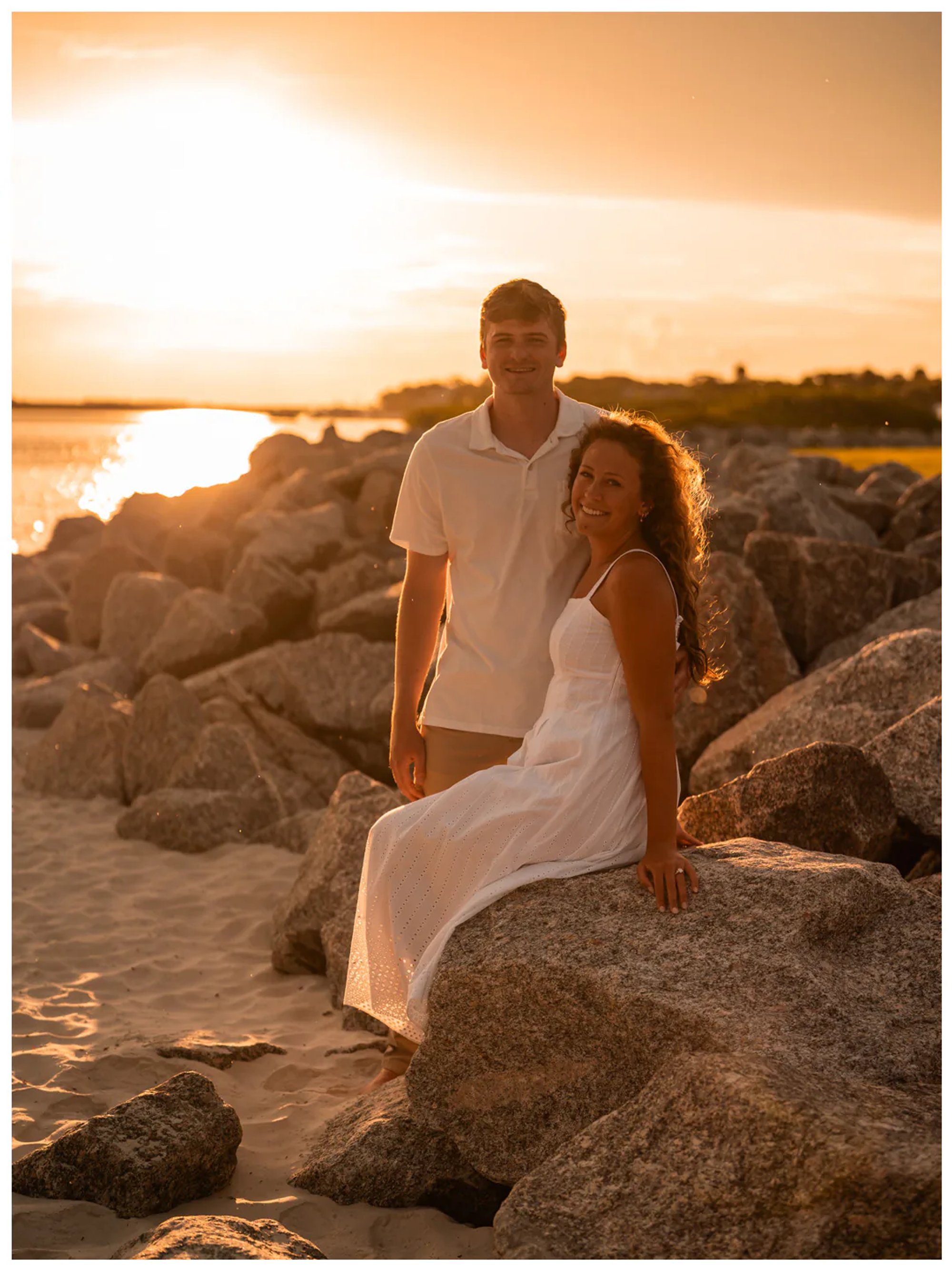 Couple seated together on shoreline rocks in golden light.