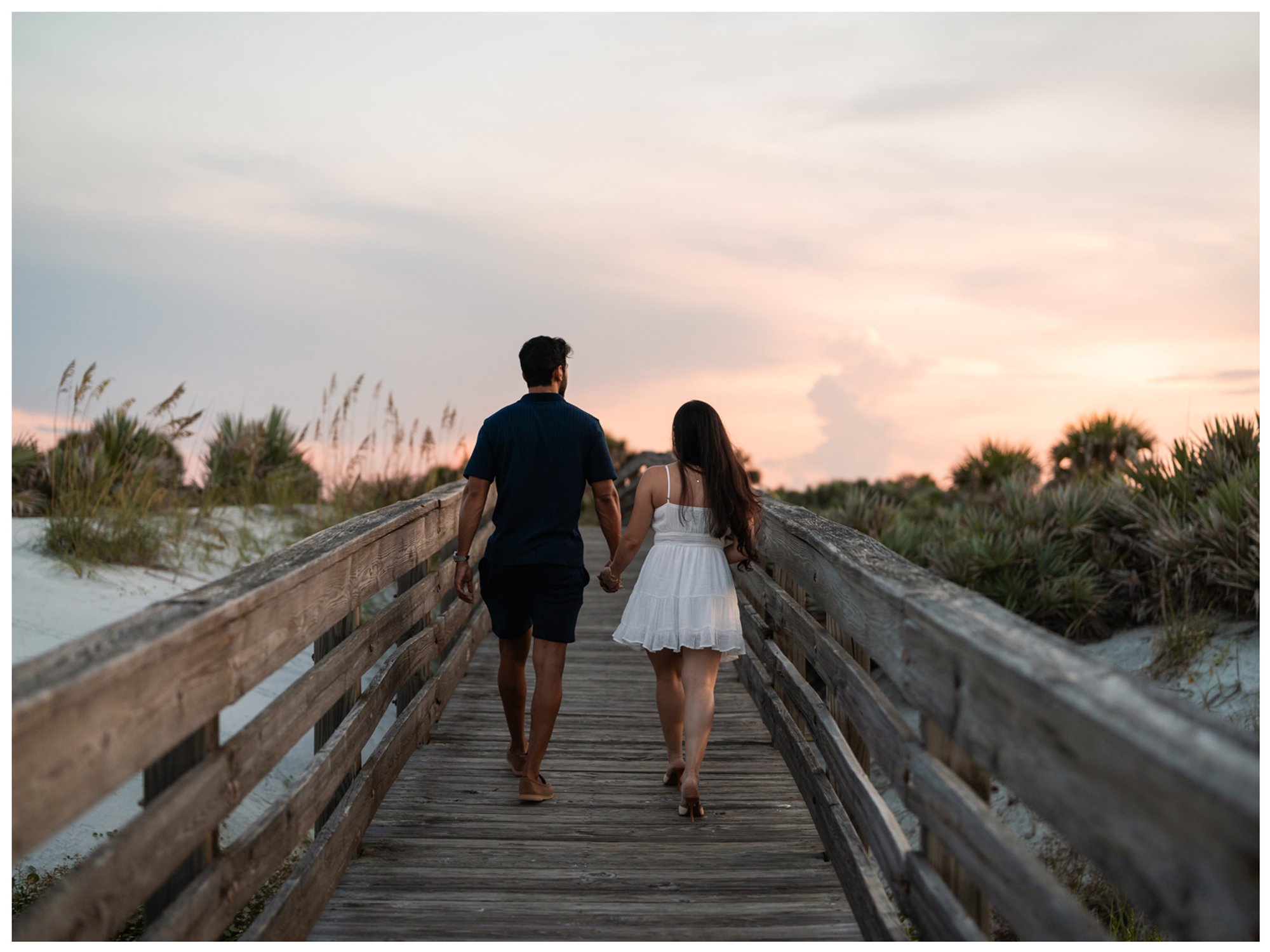 Dierick and Paulina walking hand in hand along the Lighthouse Point Park boardwalk at sunset.