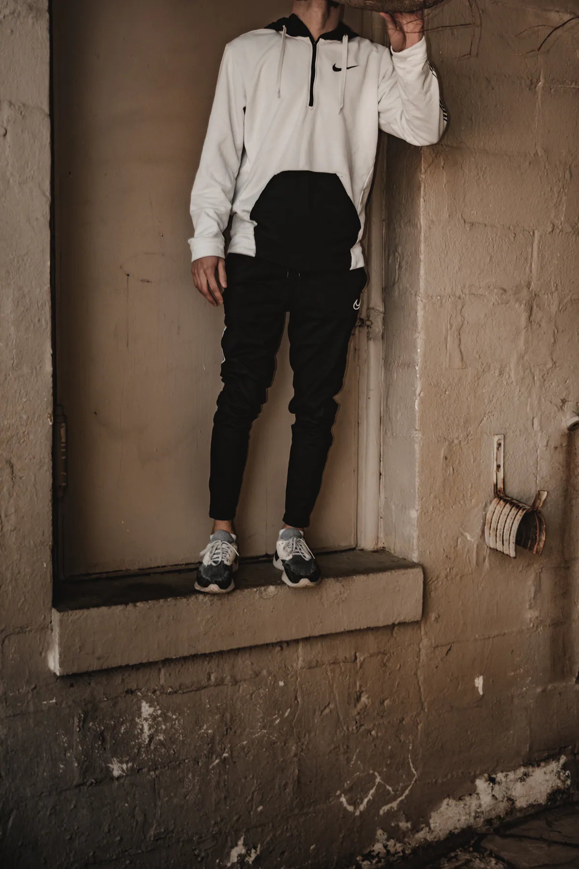 Man in a white hoodie standing on a shallow wall ledge.