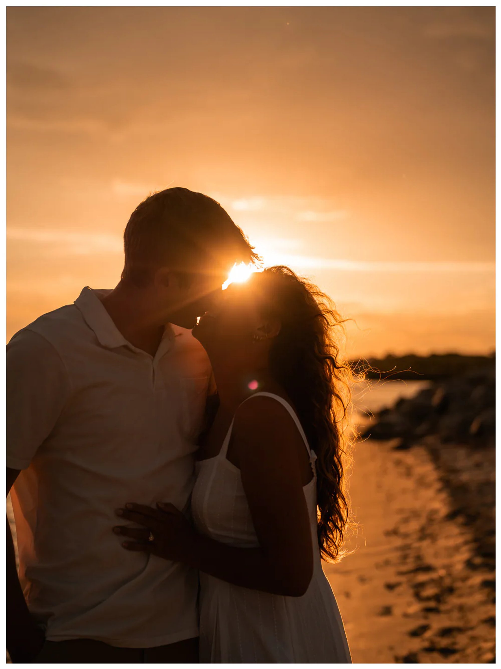 Silhouetted couple kissing with the setting sun between them.