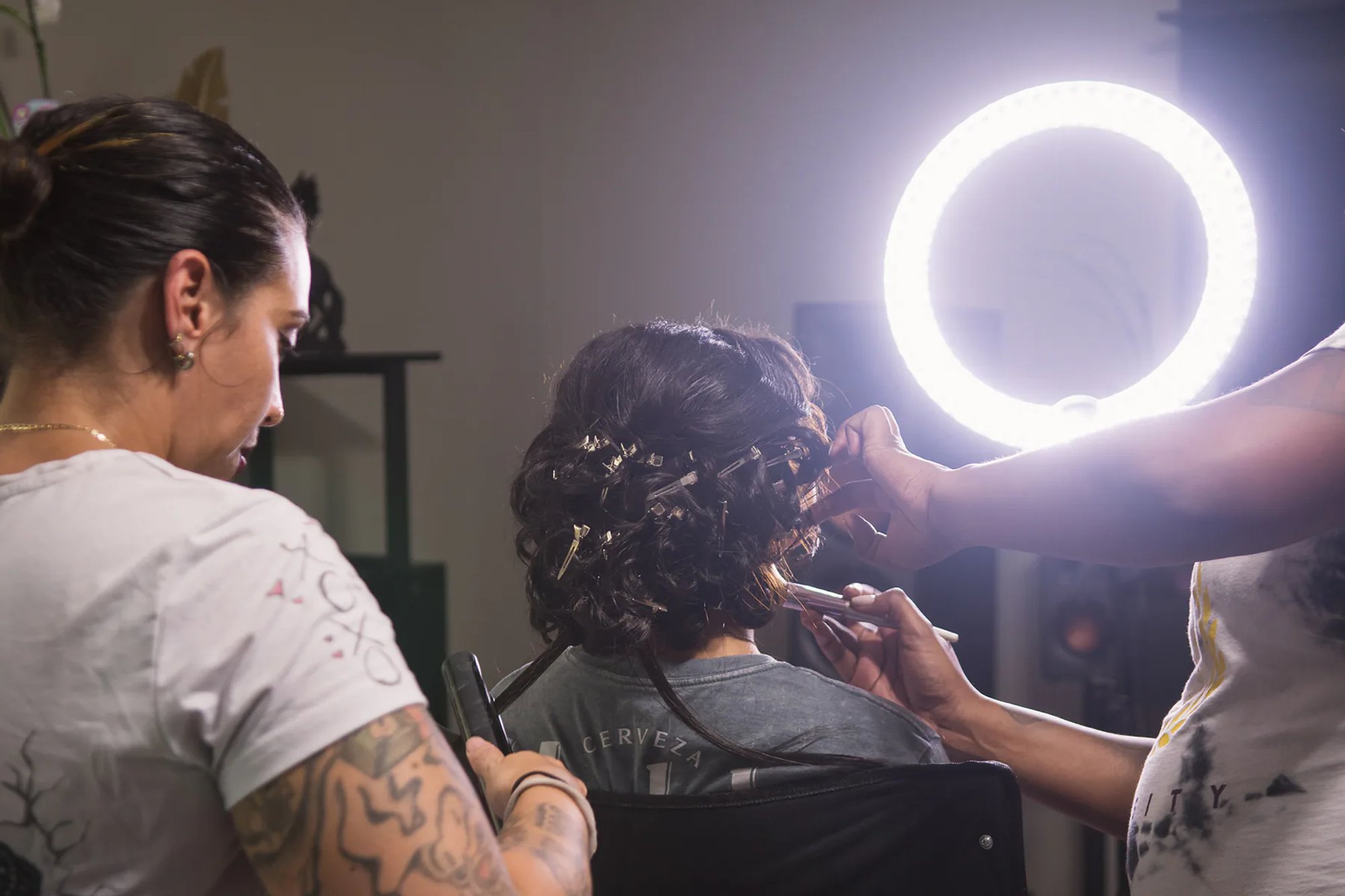 Hair and makeup artists preparing the quinceañera beneath a ring light.