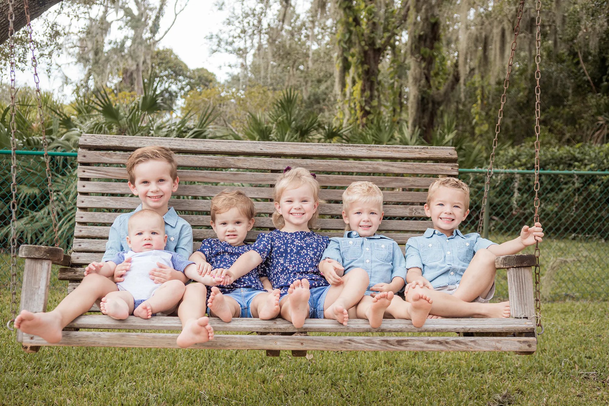 Six young children seated together on a wooden bench.