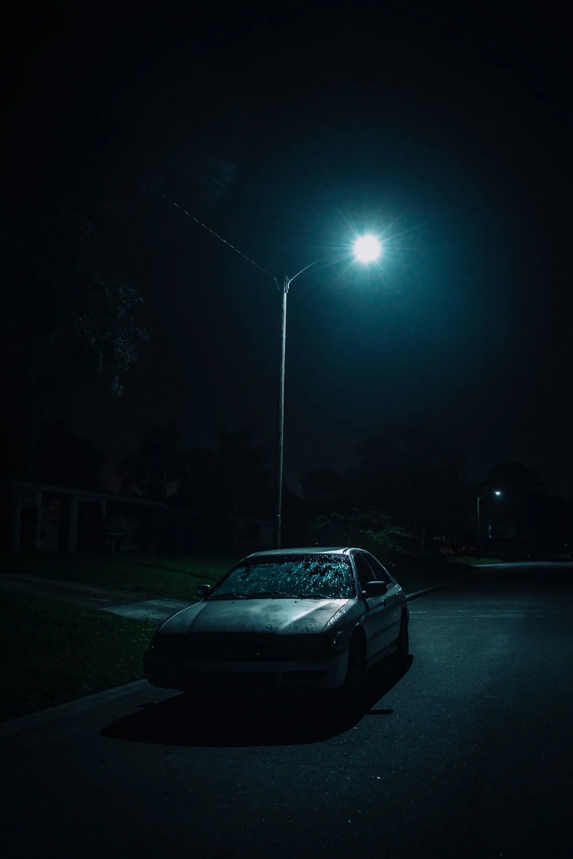 Parked car beneath a lone streetlight on a dark road.