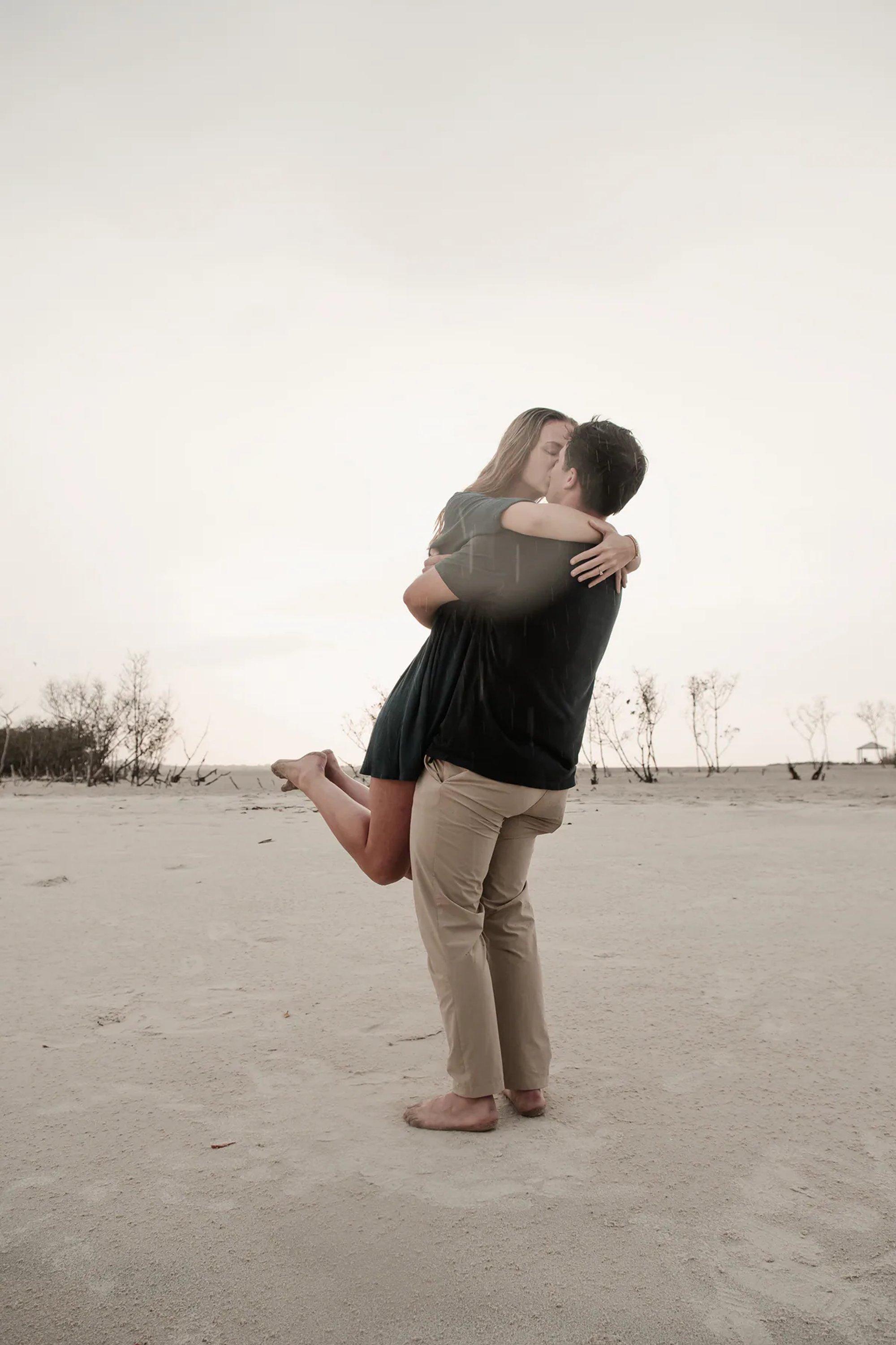 Rainy beach engagement photo of groom lifting bride-to-be at Ponce Inlet Florida