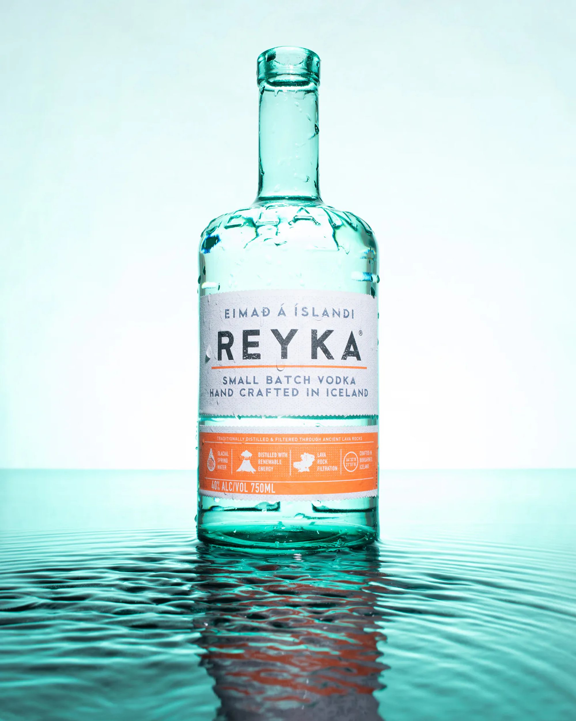 Reyka vodka bottle standing in rippling teal water.