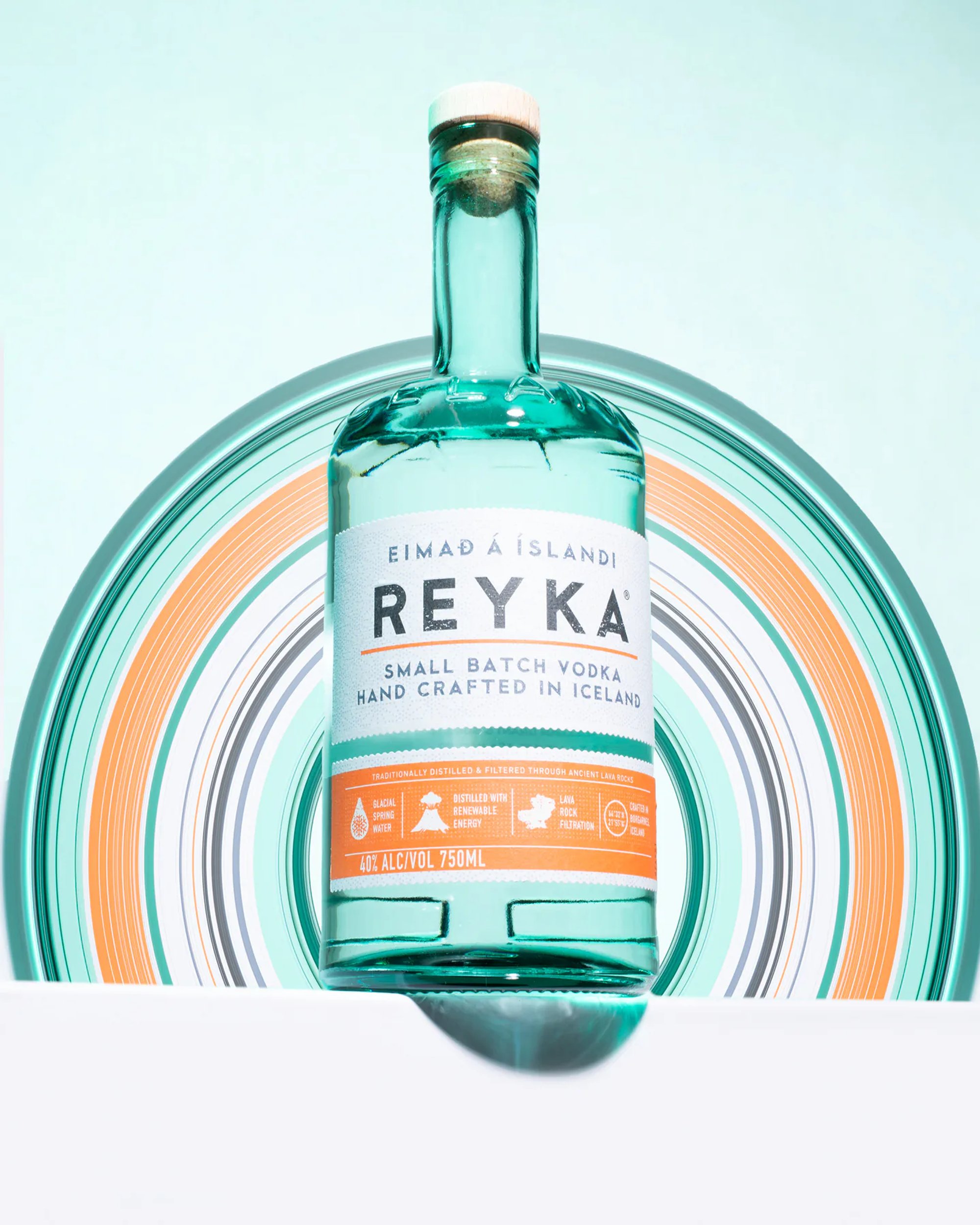 Reyka vodka bottle framed by concentric teal and orange arcs.
