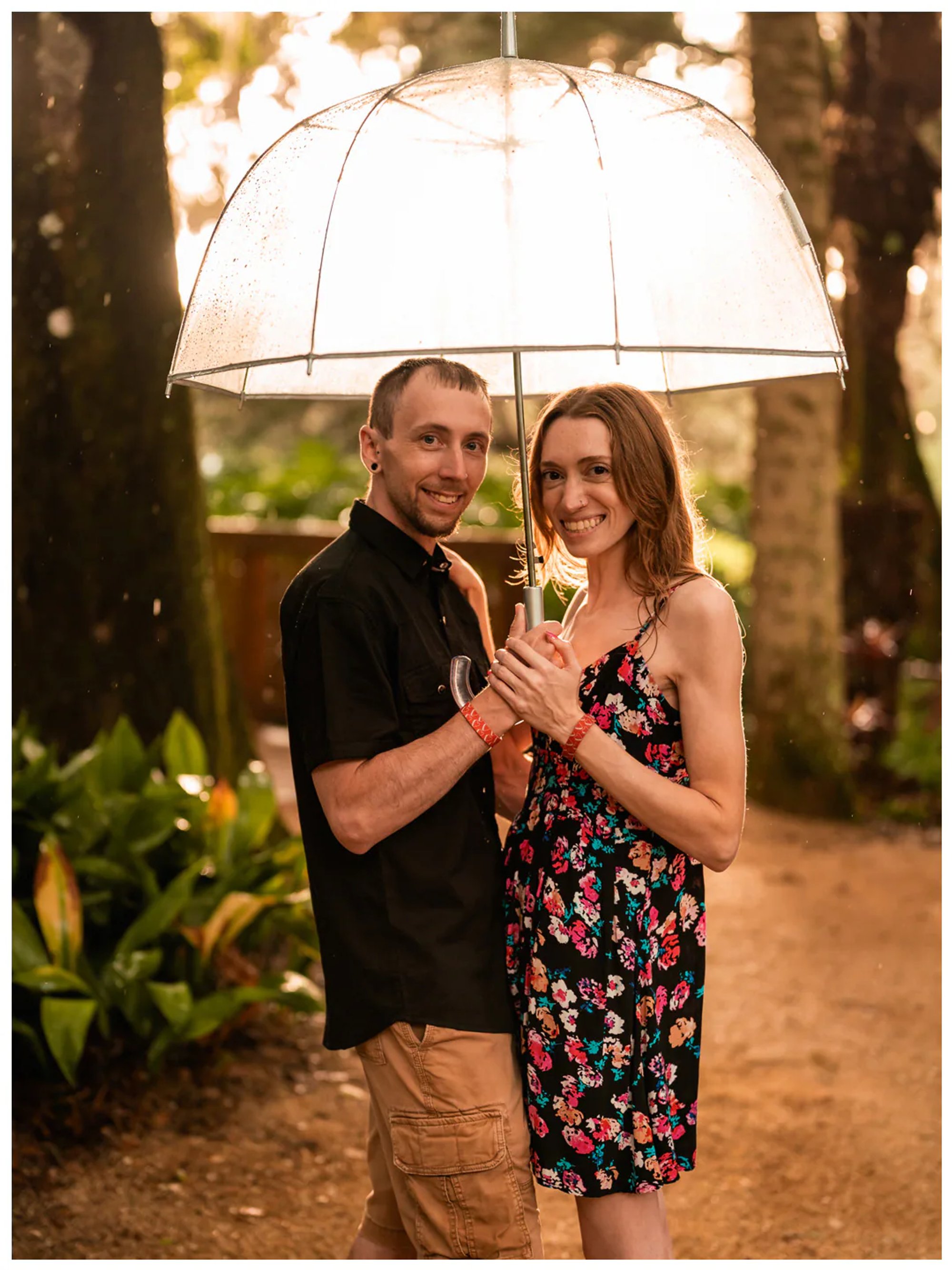 Couple smiling toward the camera beneath a clear umbrella at Washington Oaks Gardens.