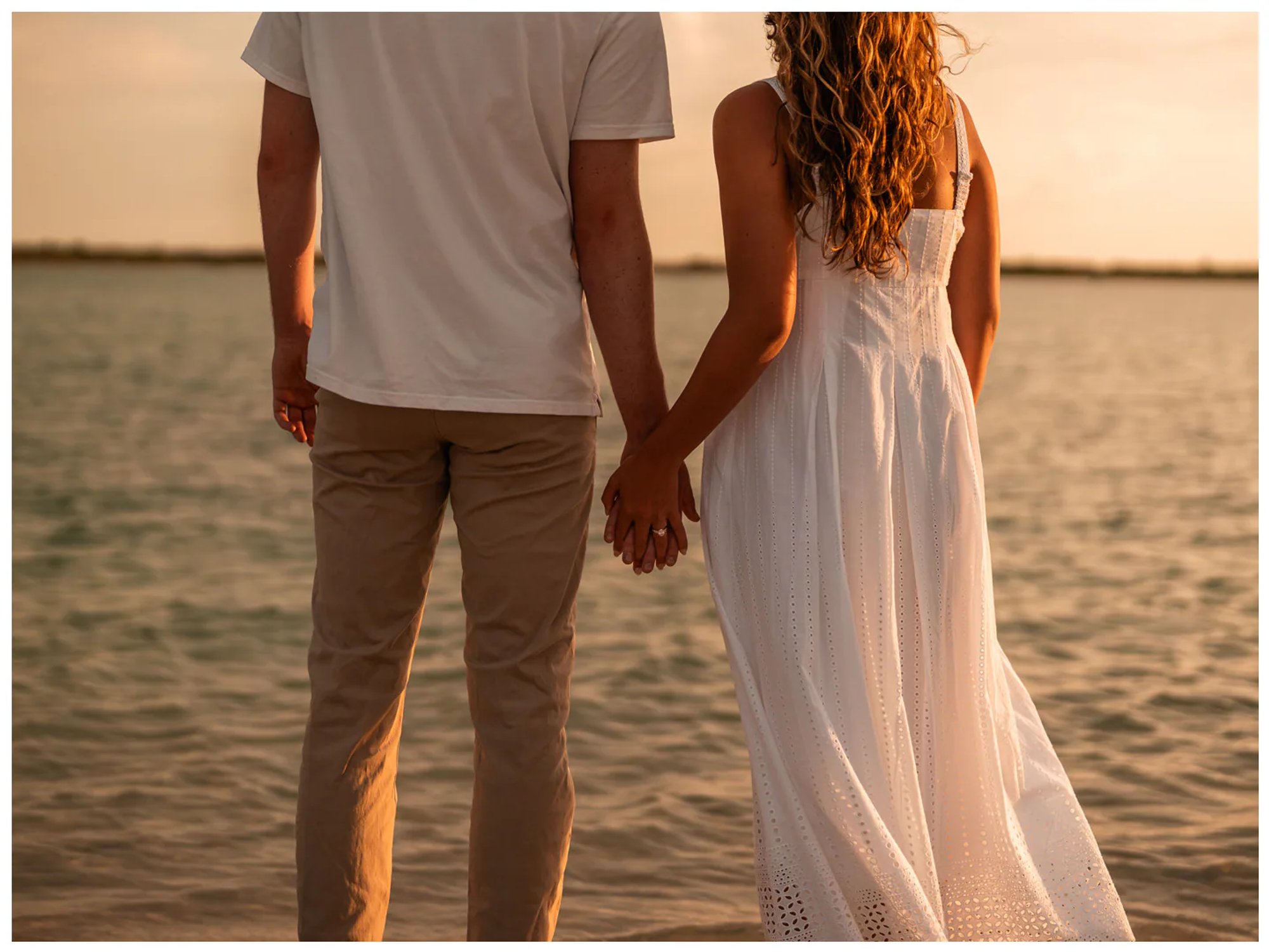 Couple holding hands while looking across the water at sunset.