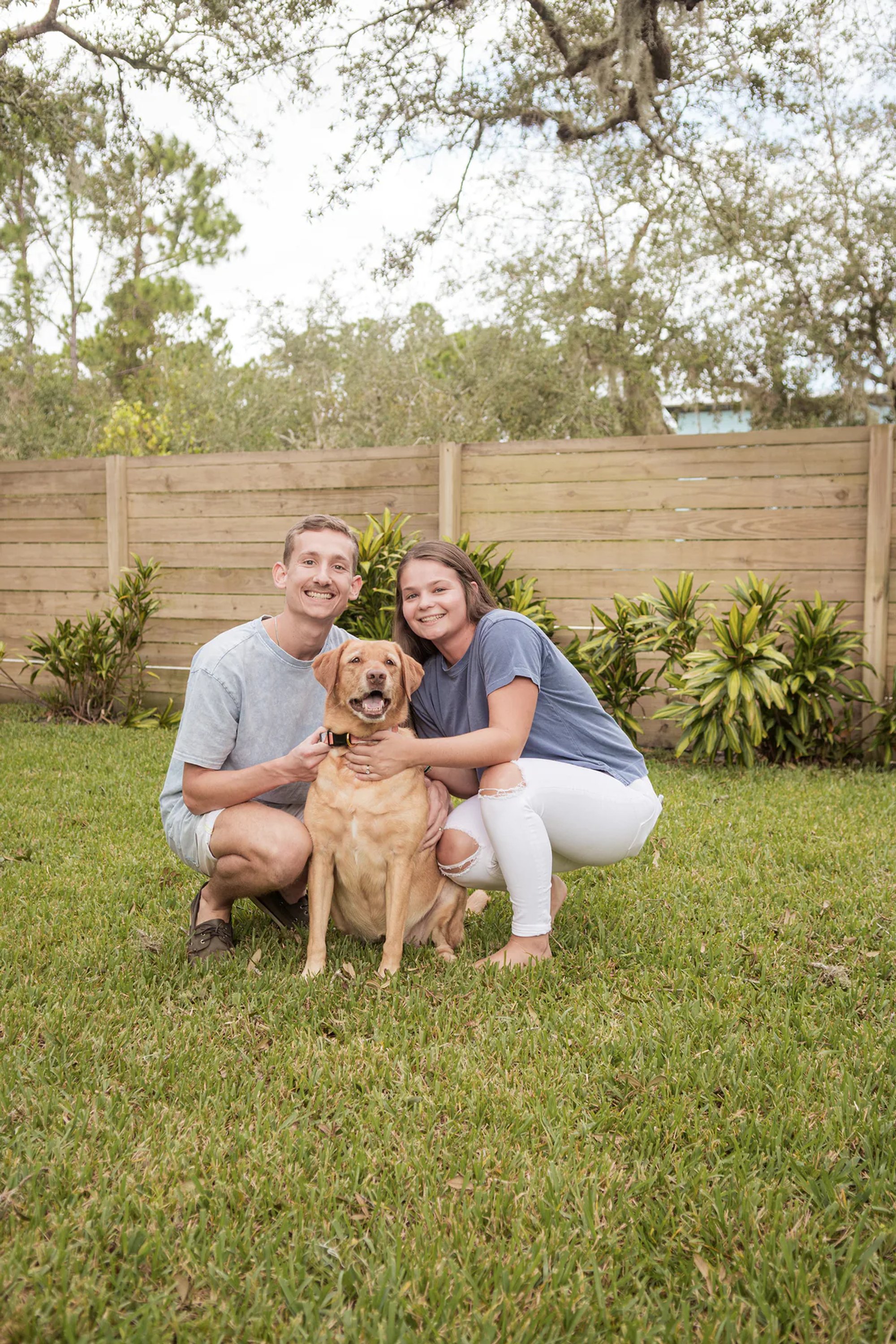 Couple crouching beside their golden retriever on the grass.