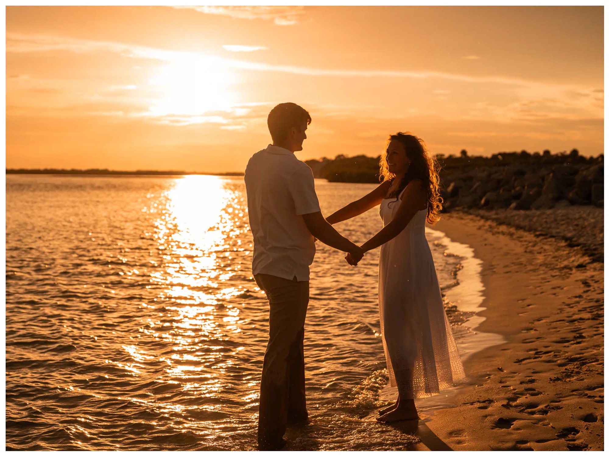Couple facing each other and holding hands beside the water.