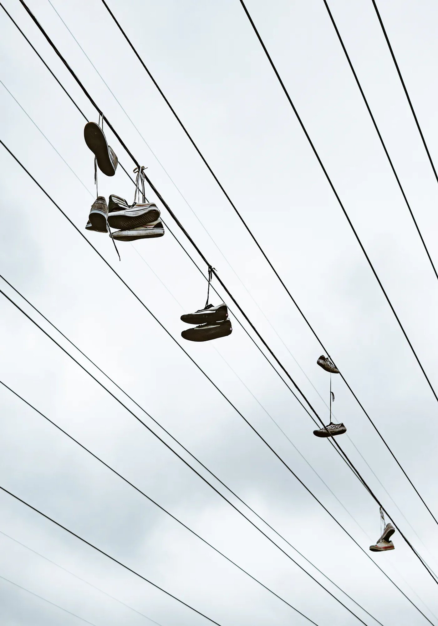 Pairs of shoes hanging from utility wires against a cloudy sky.