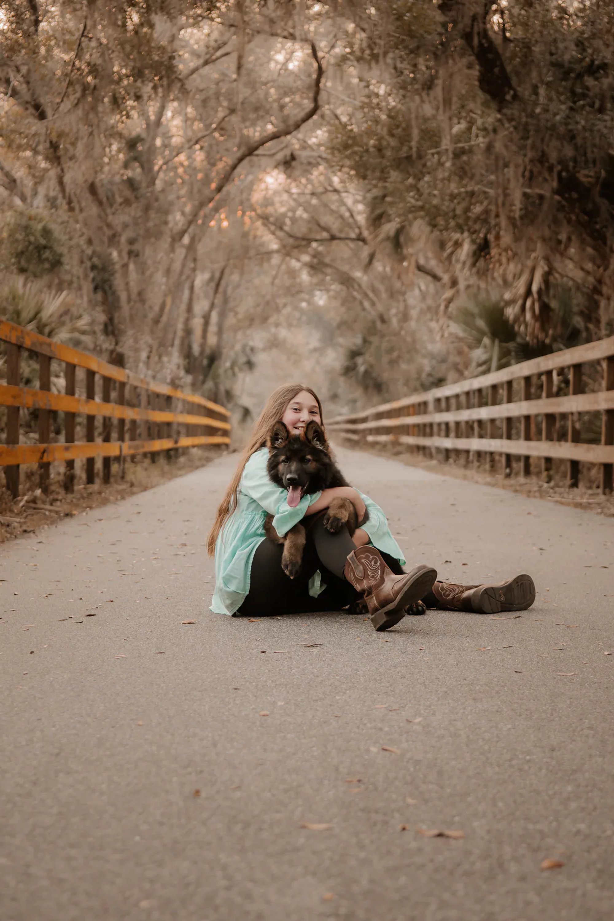 Young woman hugging her black dog on a tree-lined road.