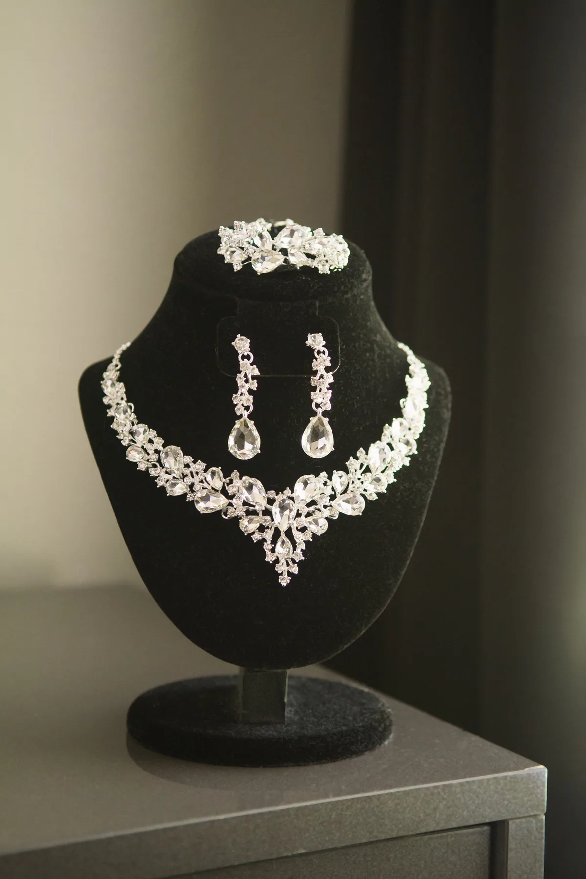 Sparkling silver jewelry set displayed on a black stand.