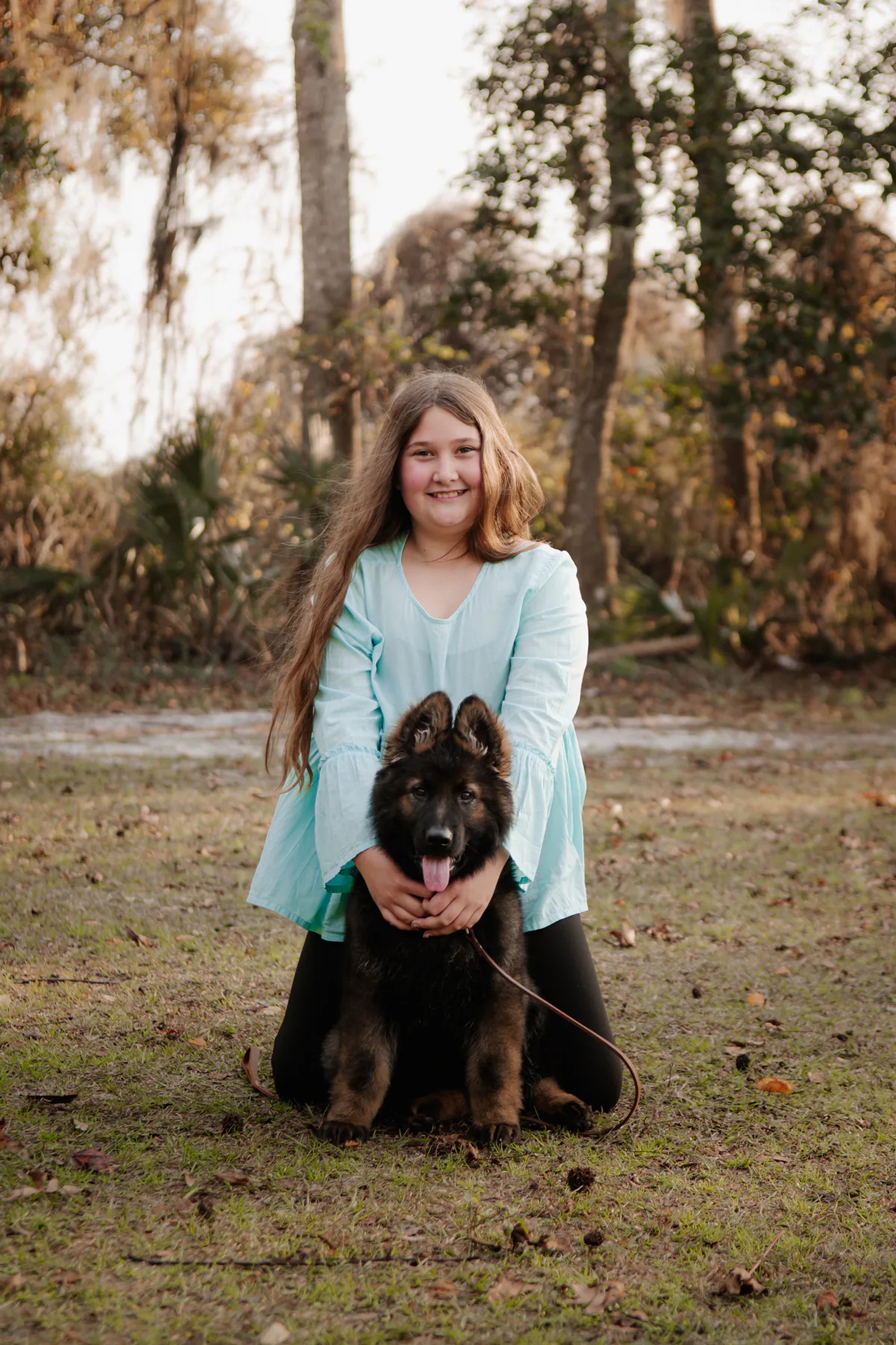 Young woman kneeling behind her fluffy black dog outdoors.