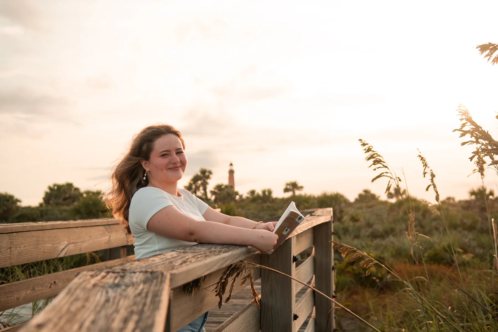 Senior portraits in Ponce Inlet FL, Nelly leaning casually on the boardwalk railing with the sun behind her.