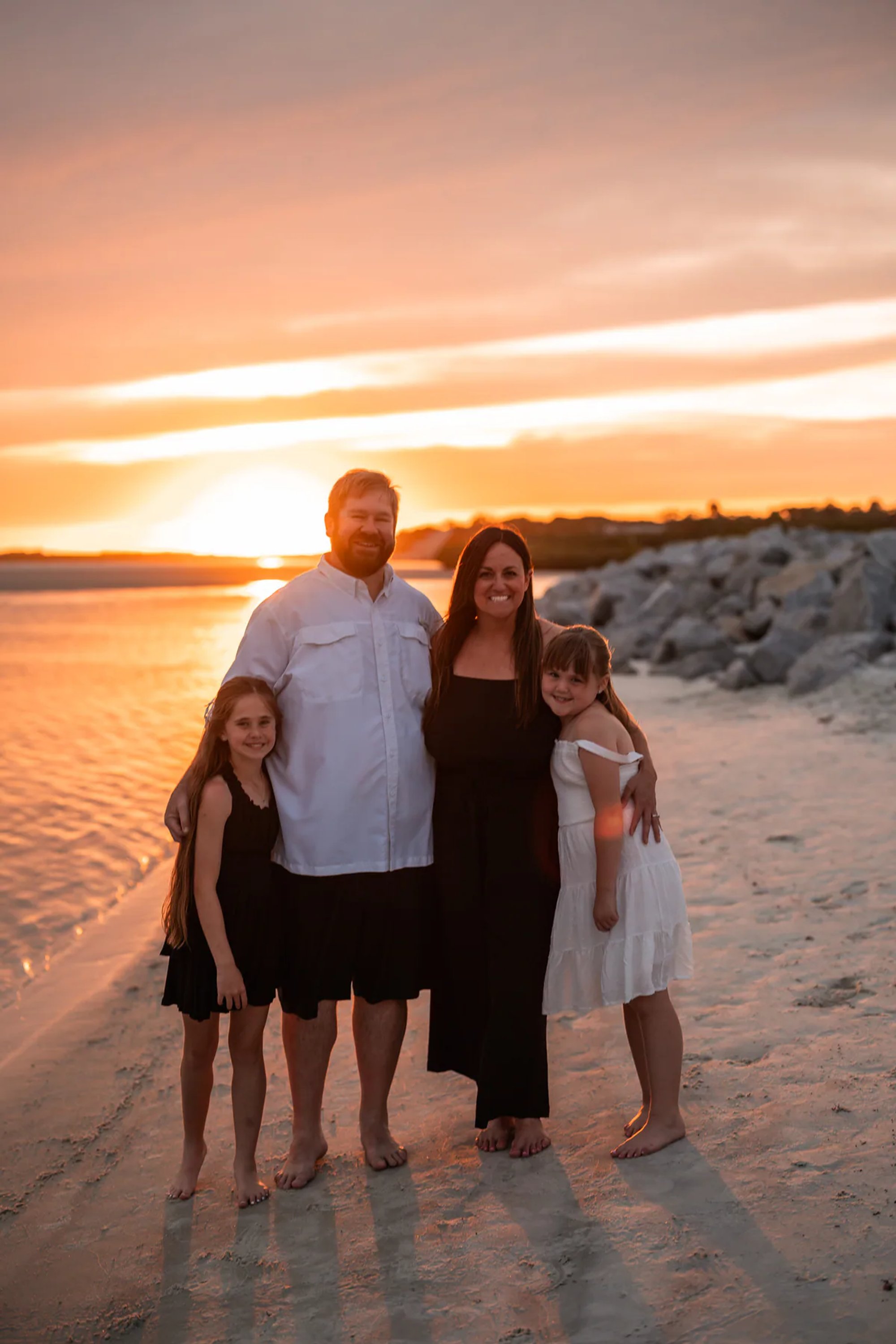 Family portrait near the rocks and shoreline during a sunset beach session in Ponce Inlet.