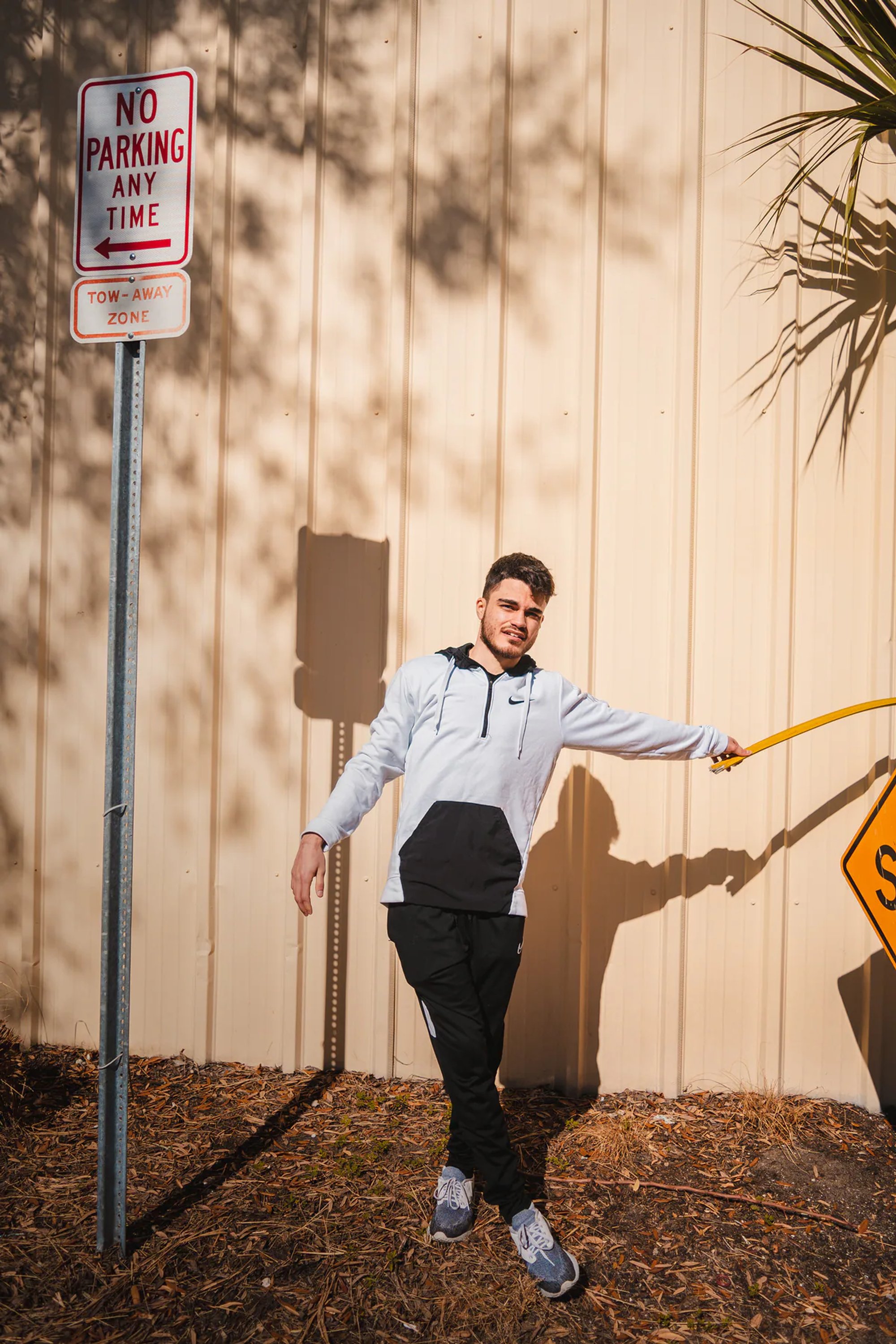Man in a bow tie and suspenders posing beside an industrial building.