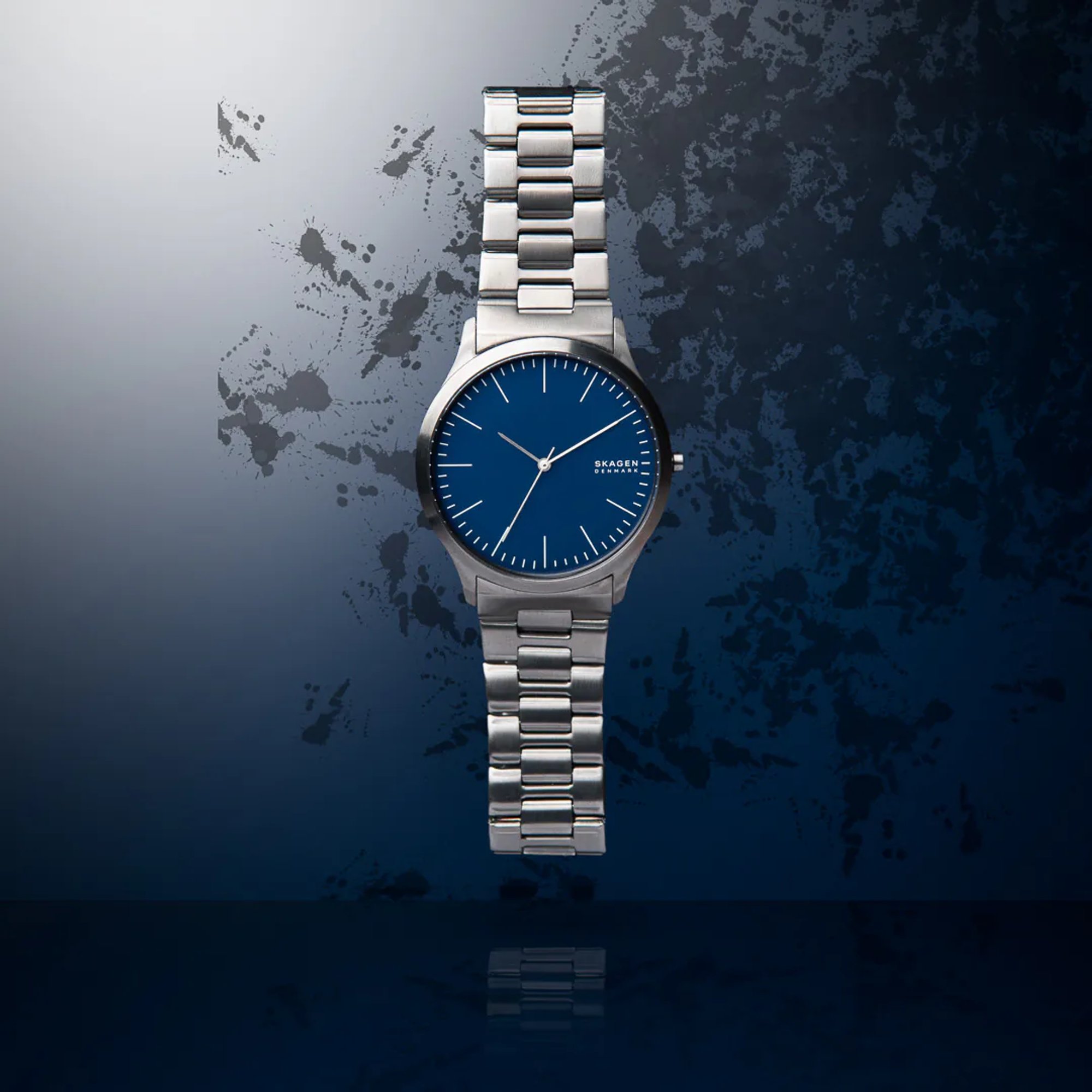 Blue-faced silver wristwatch against an abstract blue shadow.