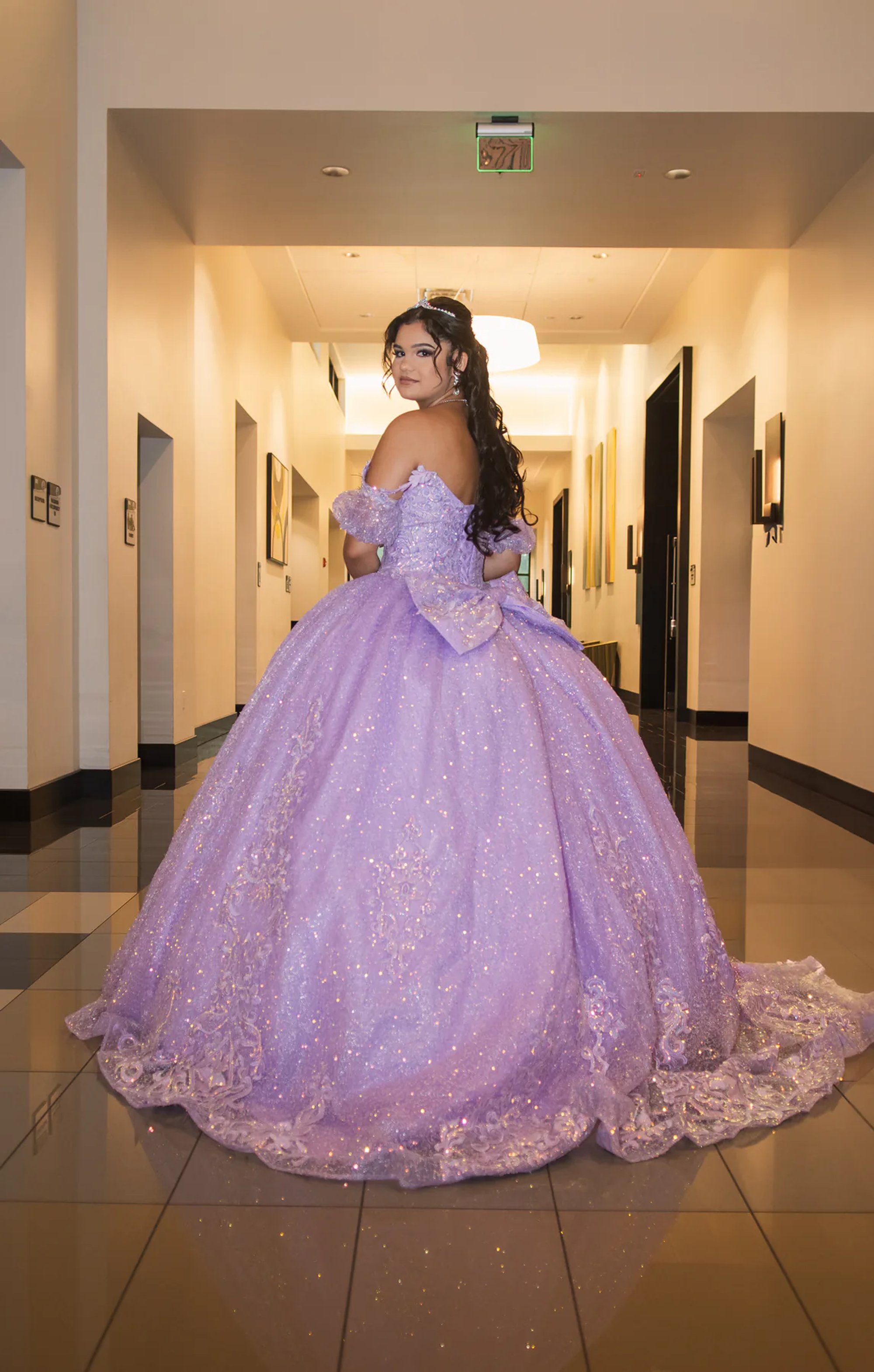 Quinceañera walking down a hallway in her full purple ball gown.
