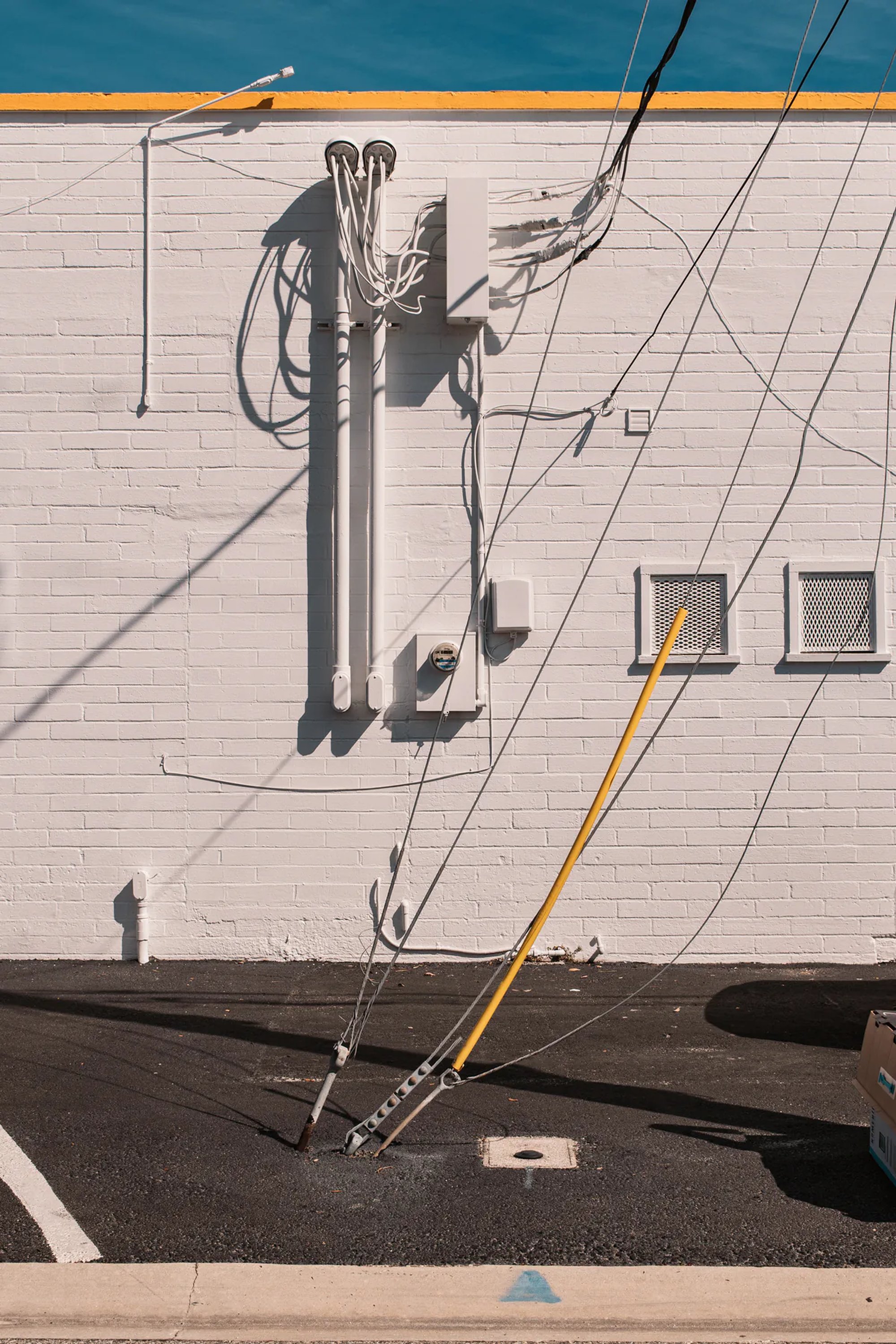 Utility lines and equipment casting shadows across a pale brick wall.