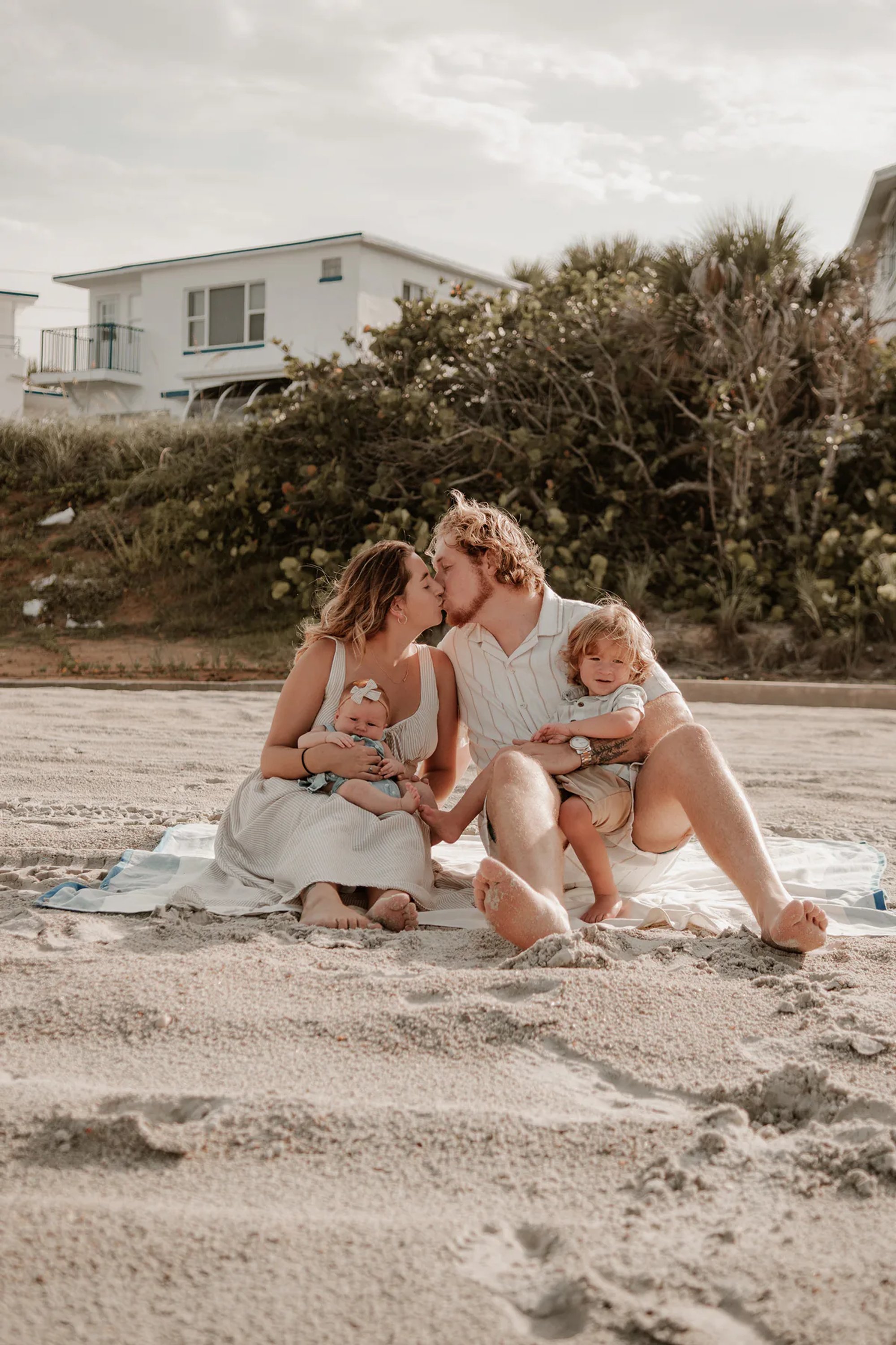 Family with two young children seated together on the sand.