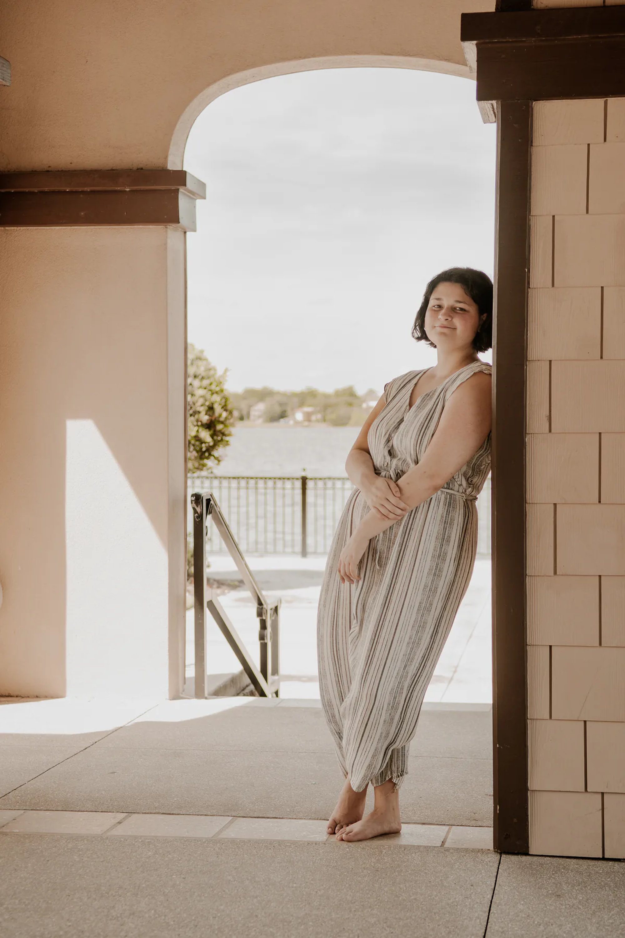 Woman in a flowing striped dress standing in a coastal archway.