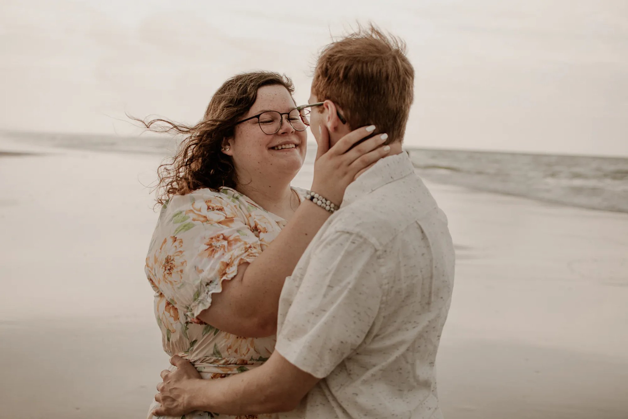 Couple embracing near the ocean with wind moving through their hair.