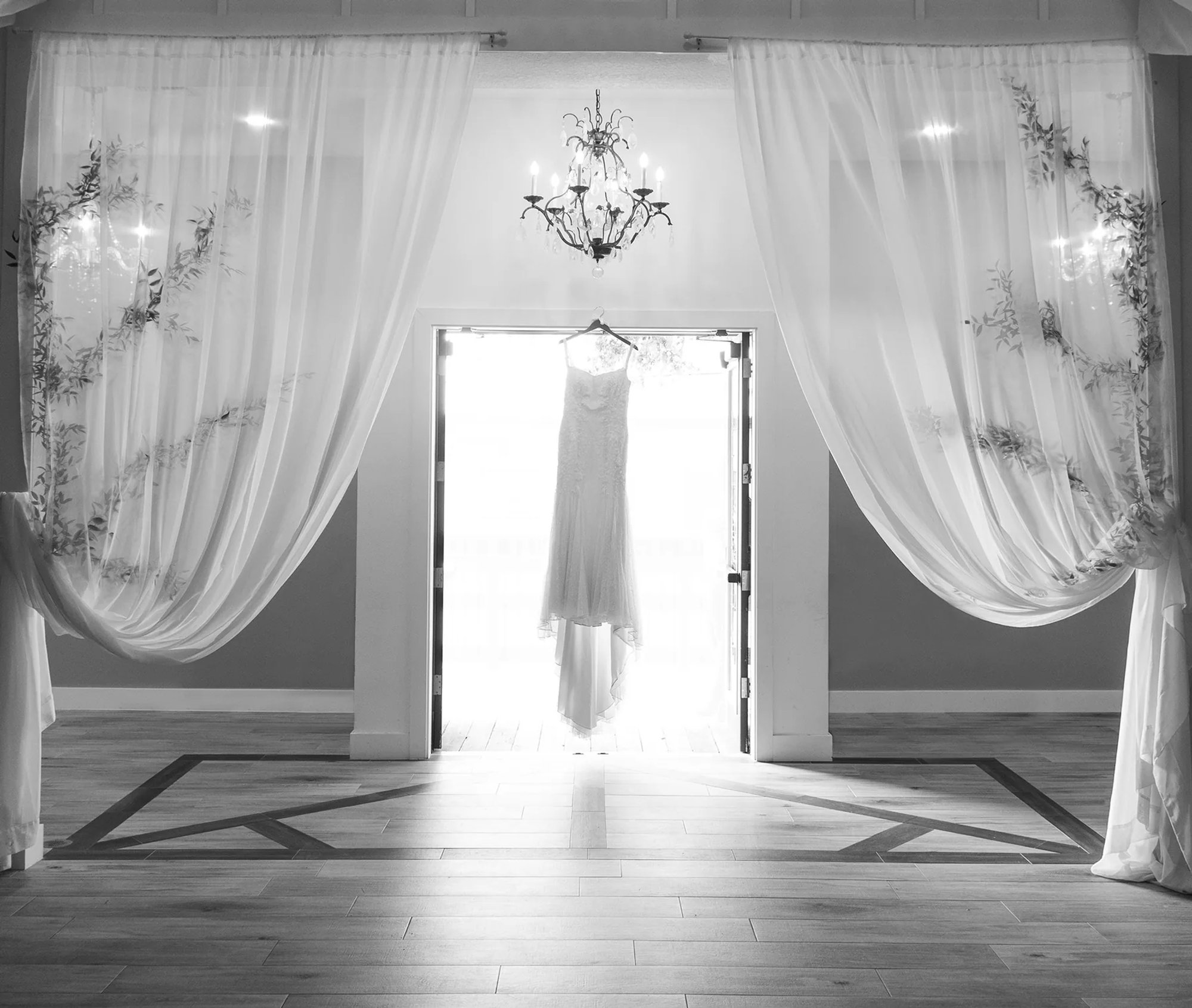 Wedding dress framed by white ceremony drapery and open doors in black and white.