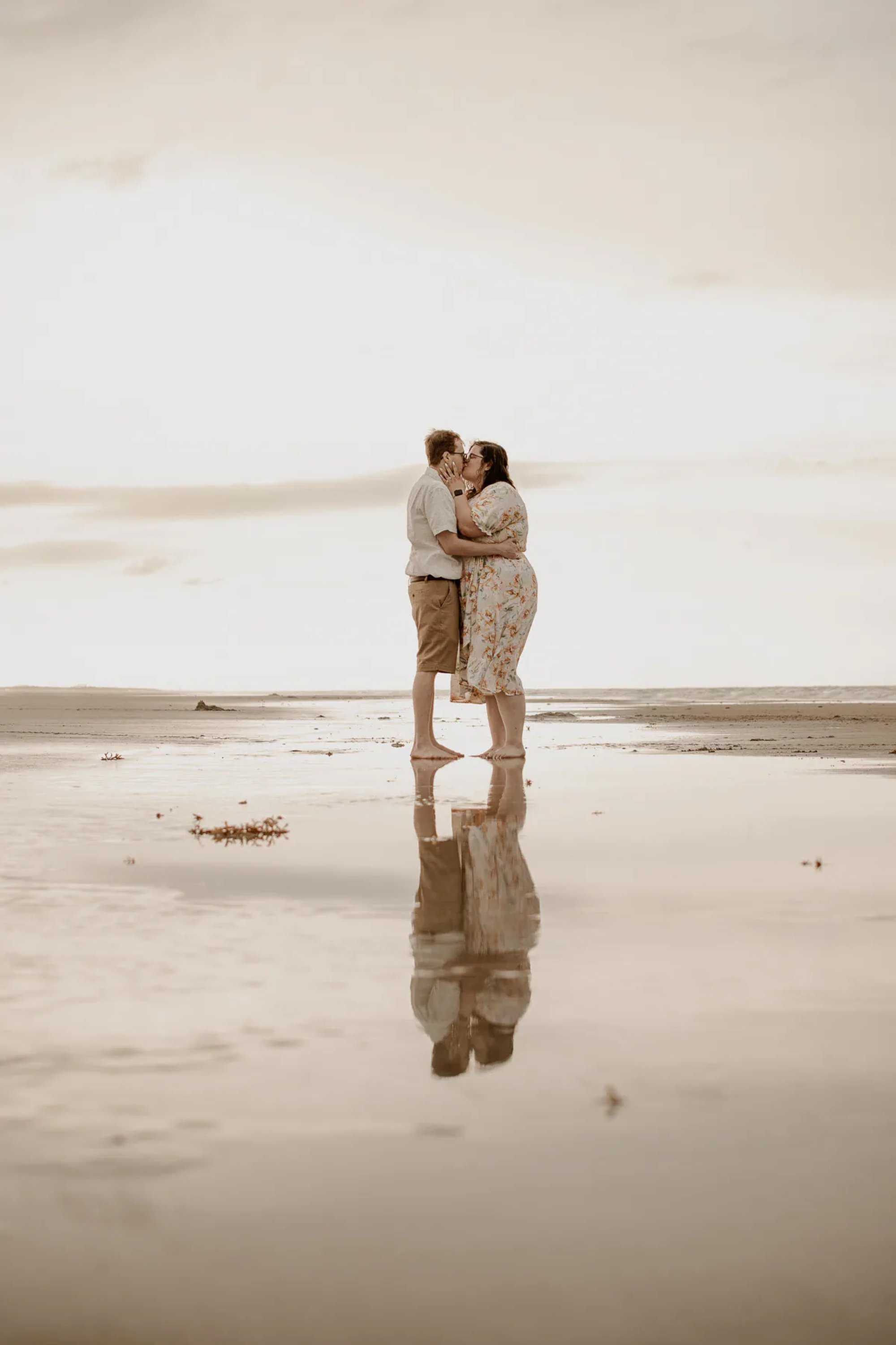 Couple embracing on wet sand with their reflection below.