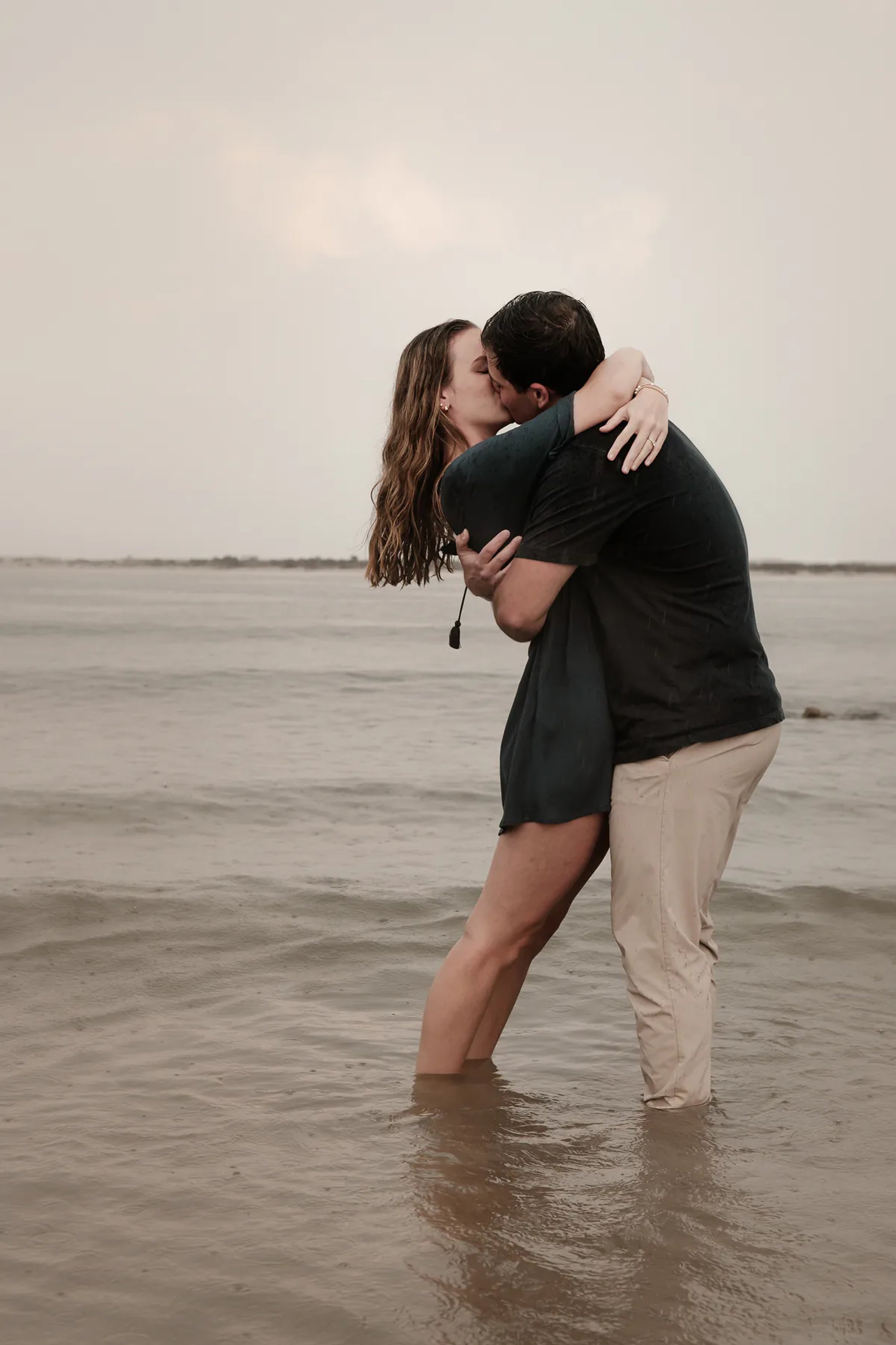 Rainy Ponce Inlet engagement photo of couple kissing in shallow water during beach session