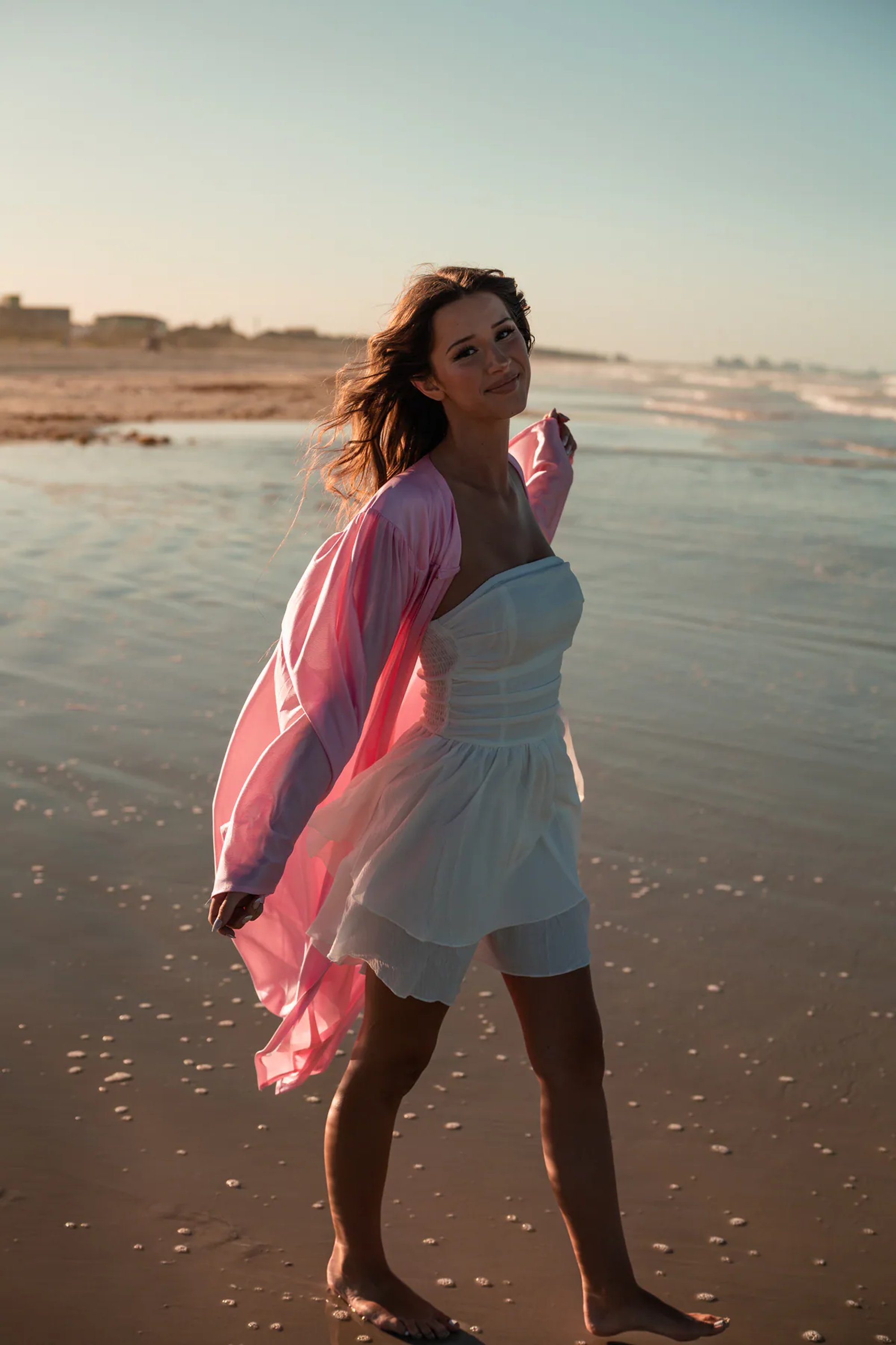 Young woman in a pink wrap walking along the shoreline.
