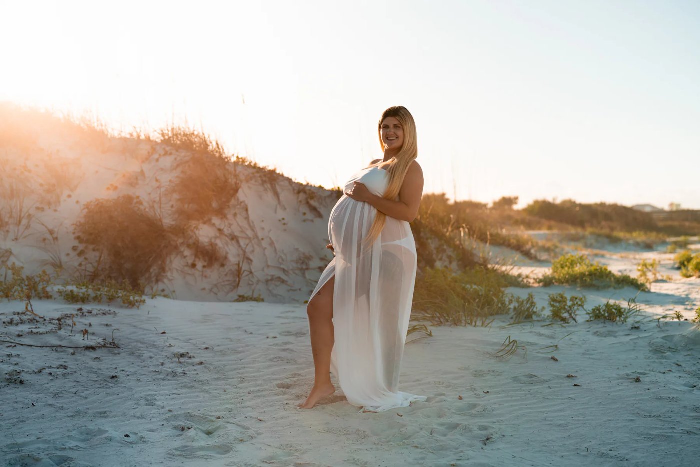 Beach maternity photo in white dress standing by the dunes in Florida