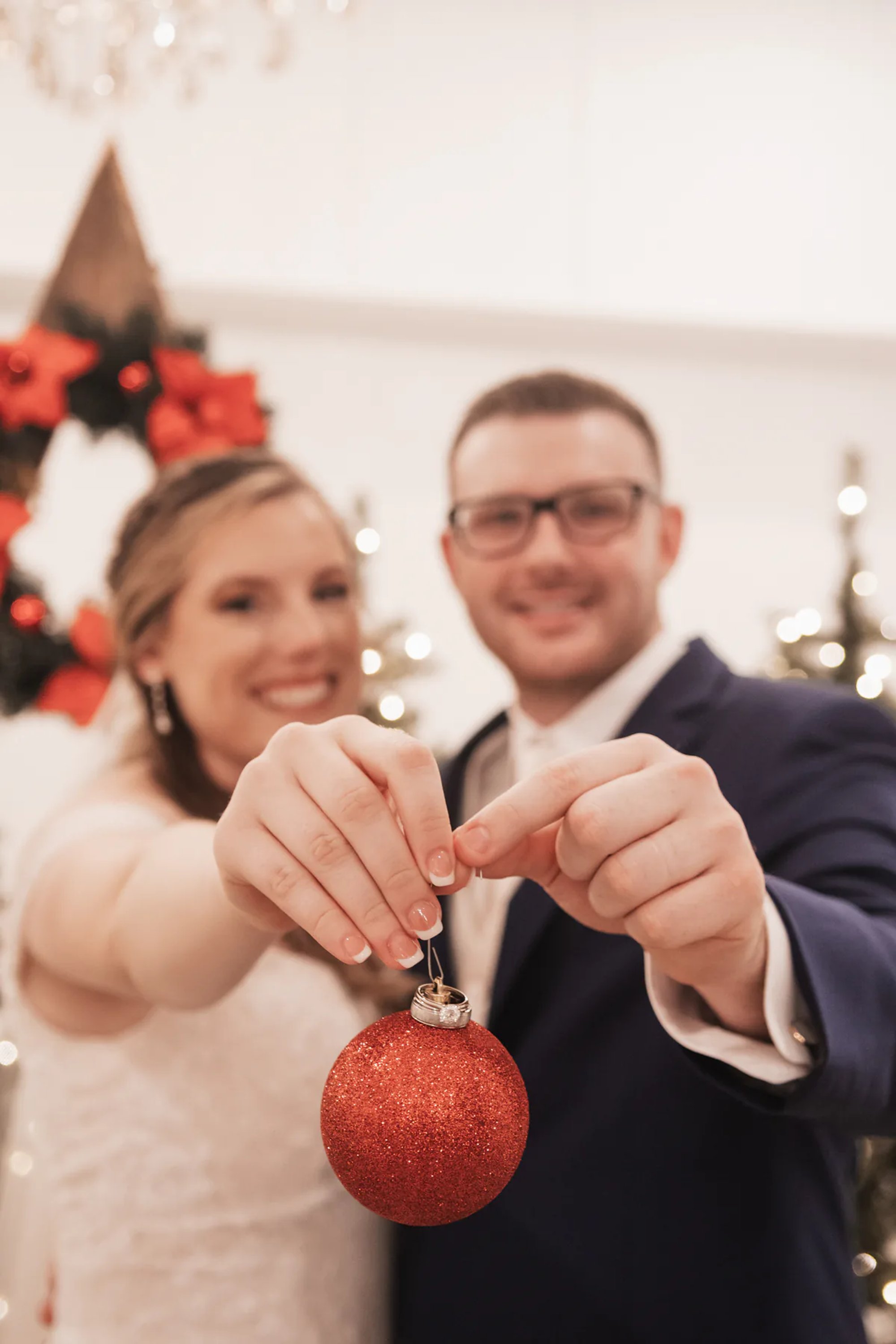 Newlyweds holding a red Christmas ornament toward the camera.
