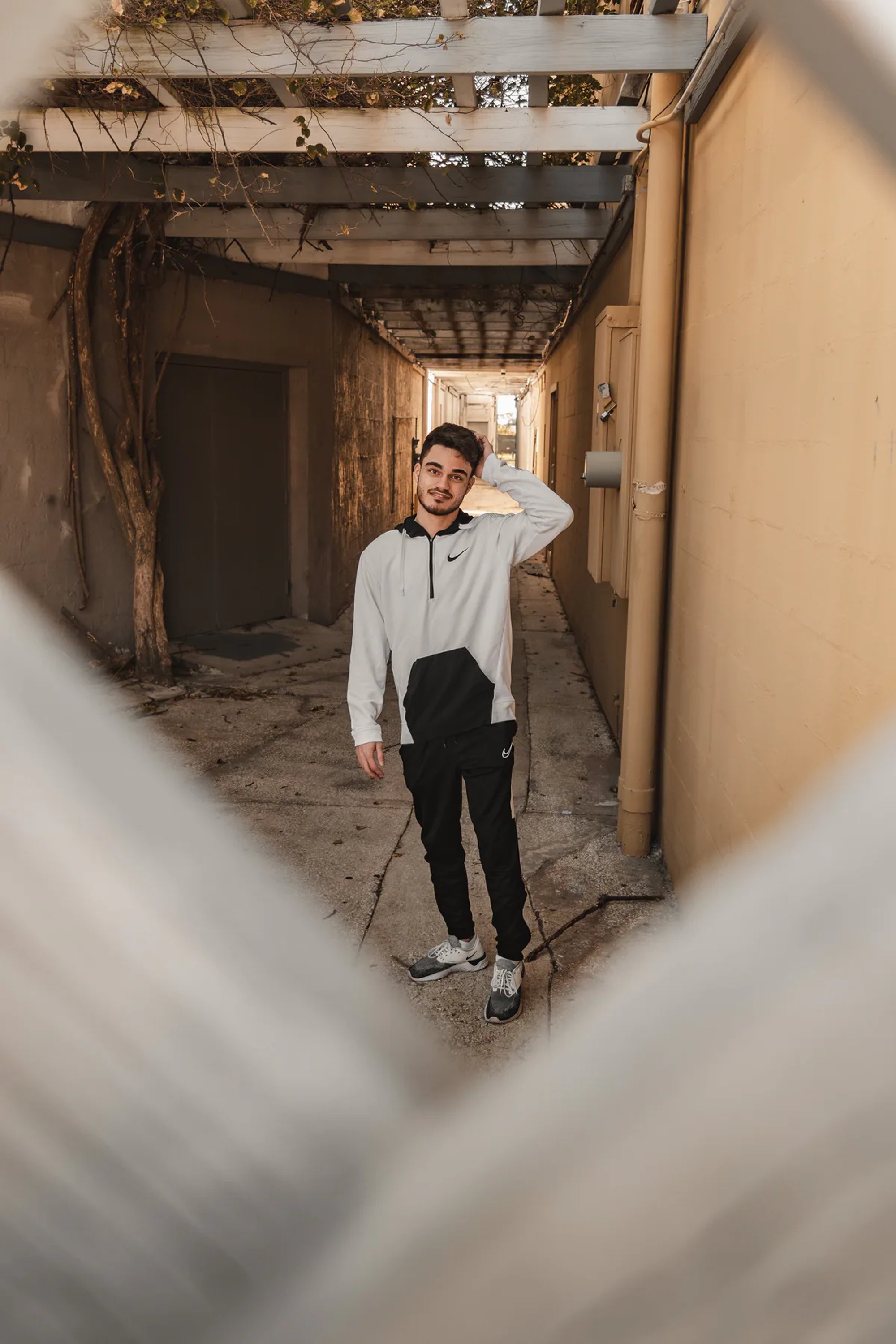 Man in a white hoodie posing in a narrow outdoor passage.