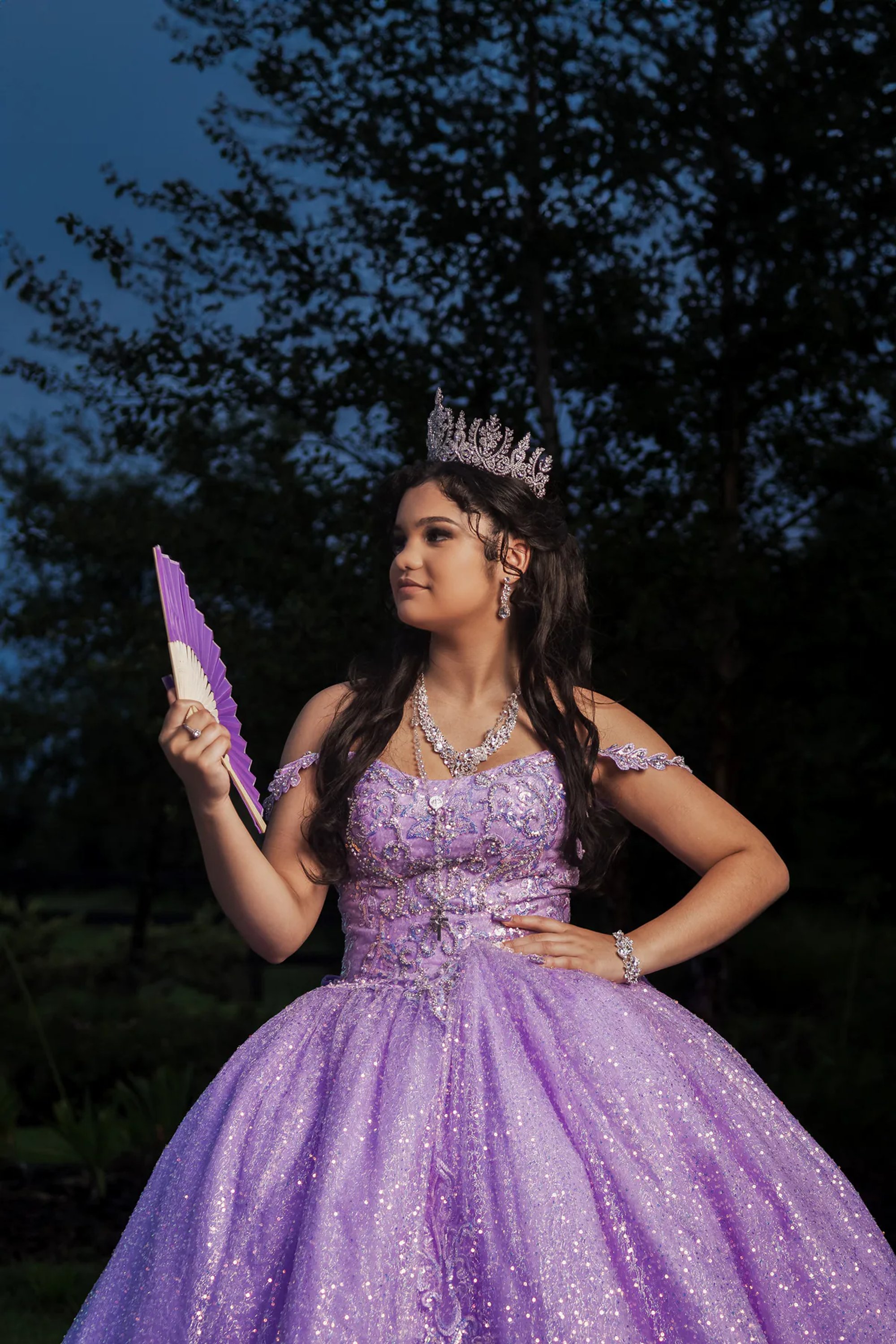 Quinceañera in a sparkling purple gown holding a folding fan.
