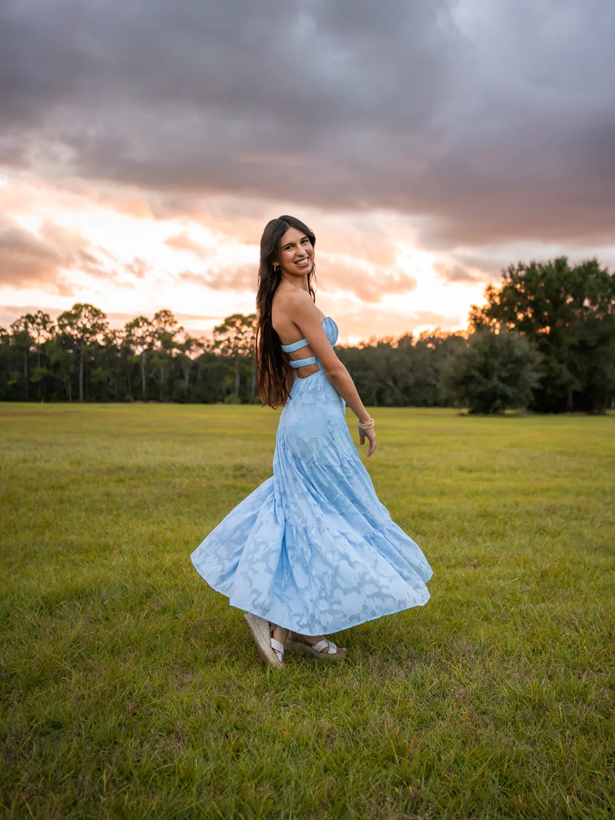 Young woman twirling her pale blue dress in a grassy field.