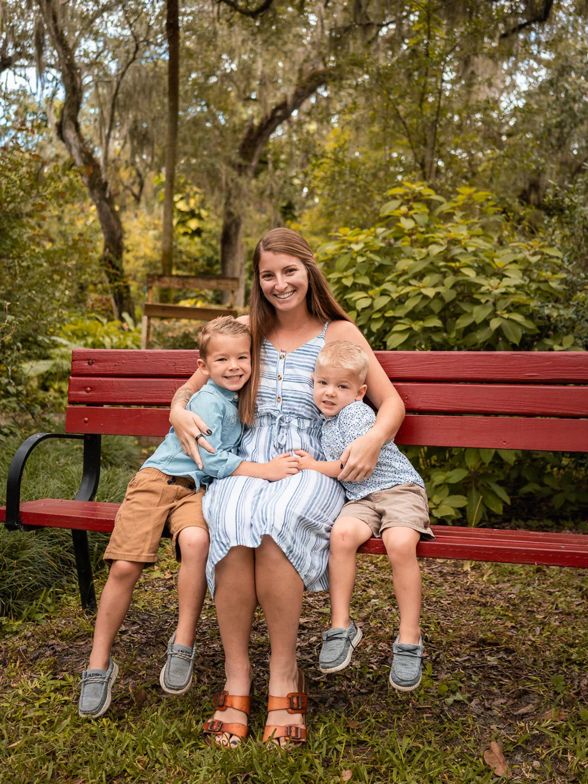 Mom sitting on a red bench holding her two youngest sons during family portraits in Port Orange, Florida.