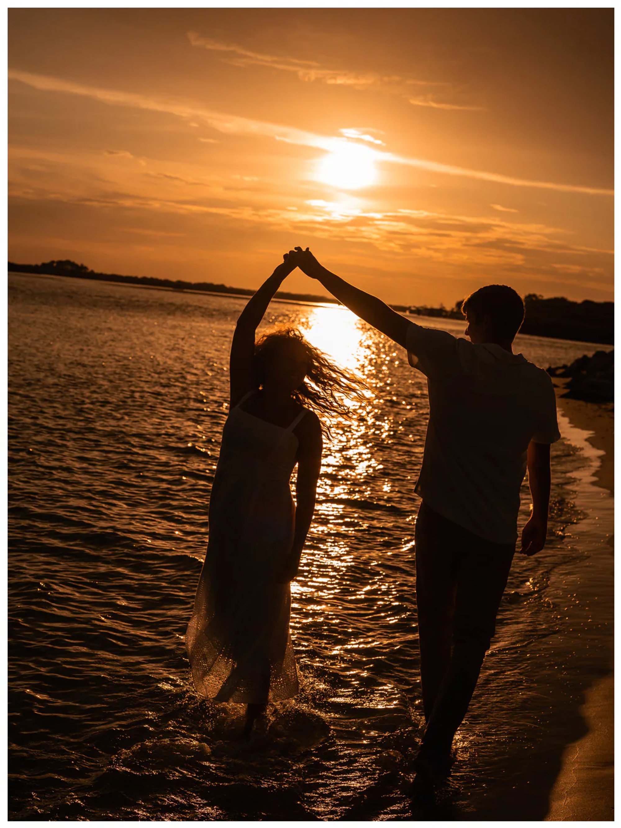 Silhouetted couple dancing in shallow water beneath the setting sun.